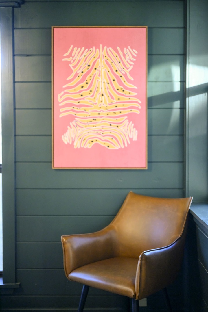 Sink into this stylish leather chair beneath vibrant artwork—your perfect corner for morning coffee or quiet moments.
