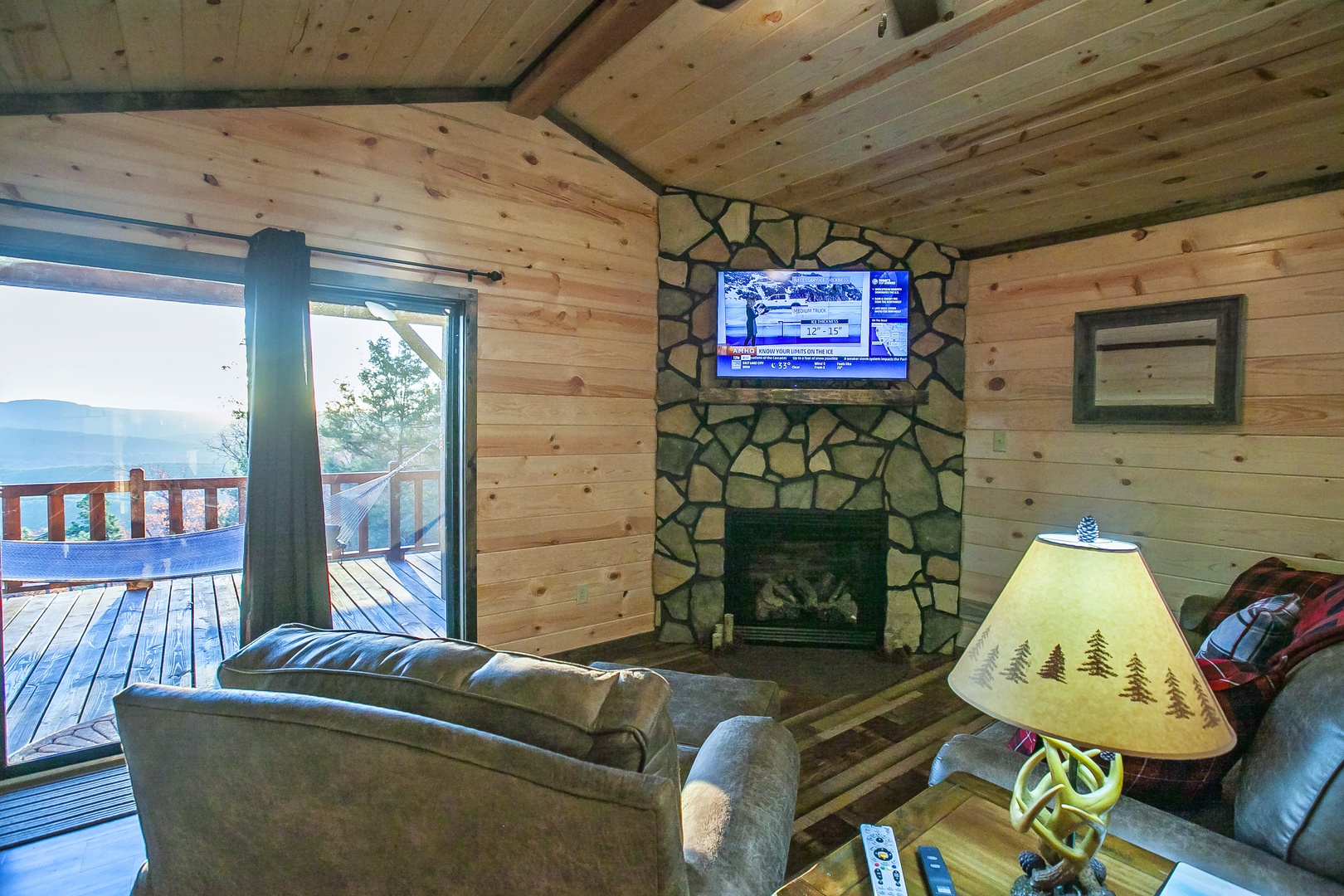 Unwind in your cozy log cabin living room with plush seating, stone fireplace, and deck views for perfect mountain getaways.