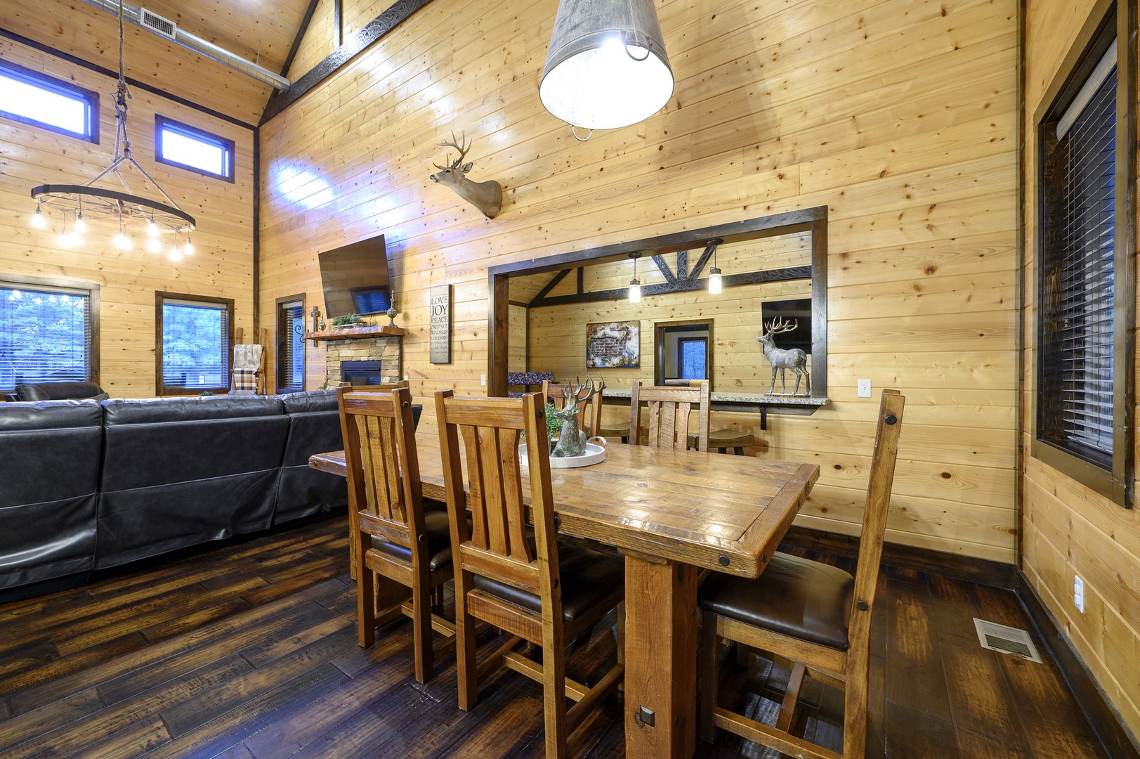 Gather around the solid wood dining table under soaring vaulted ceilings with rustic chandeliers, where warm pine walls and rich hardwood floors create your perfect mountain retreat atmosphere.