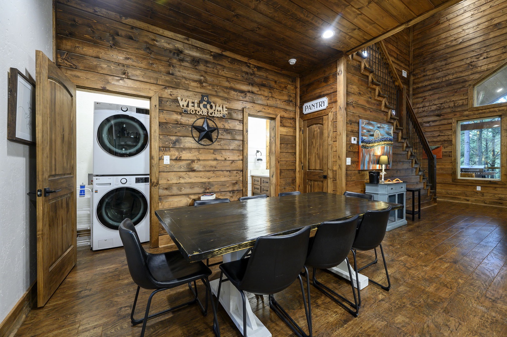 A warm cabin-style dining area with rustic wood walls and a long table ready for your group gatherings, plus convenient laundry access nearby.