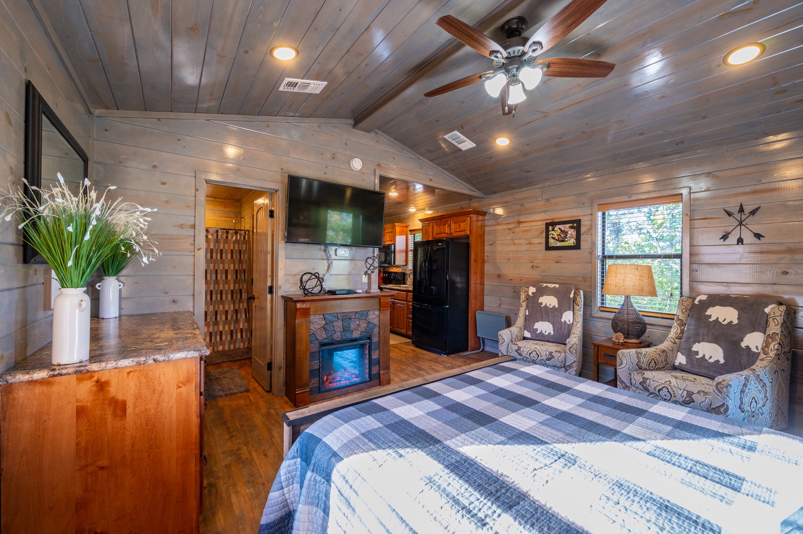 Cozy rustic charm awaits in your spacious bedroom with warm wood walls, crackling fireplace, and modern amenities perfectly blended for your comfort.