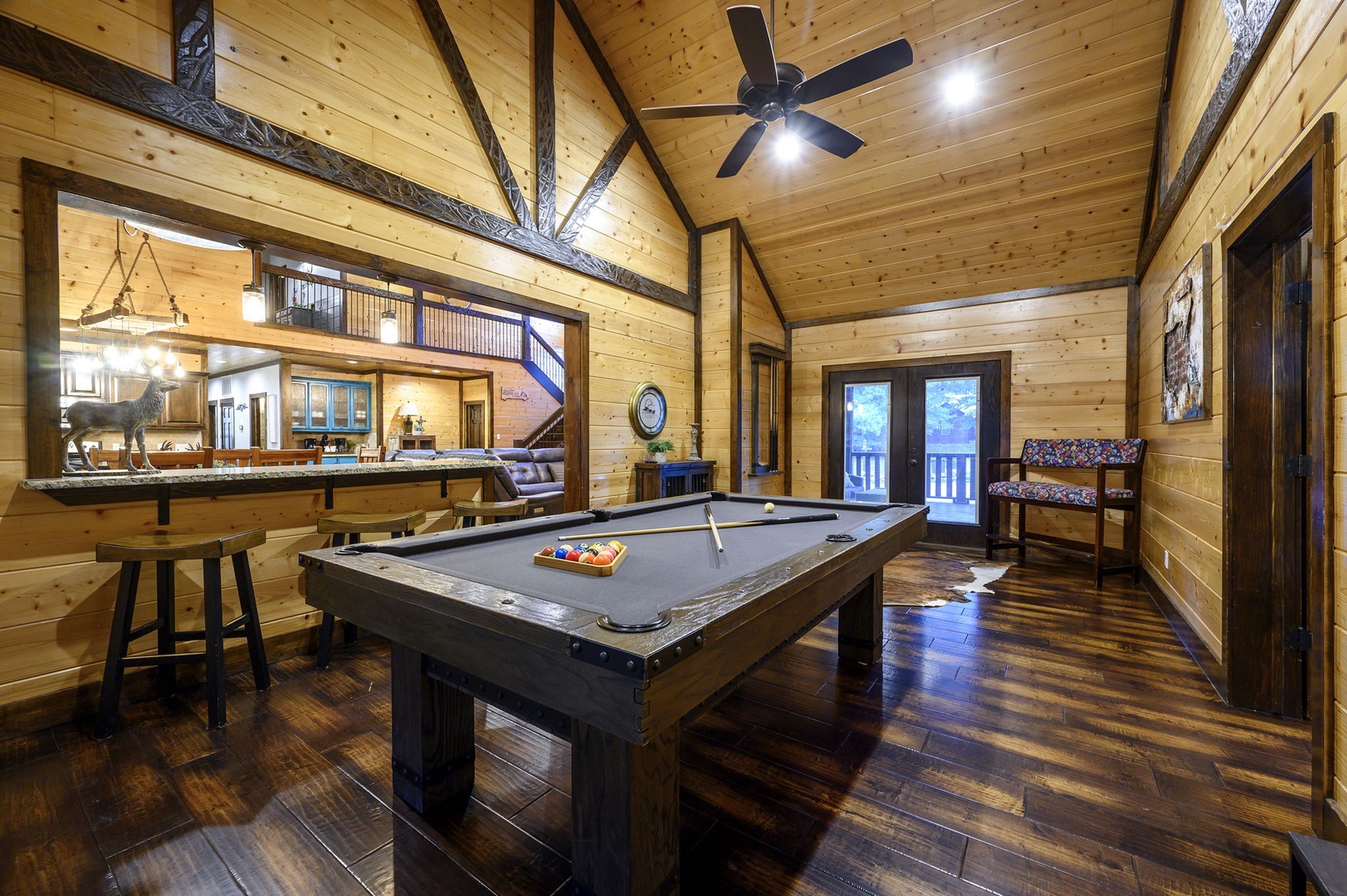 Step into your personal game room where a rustic pool table takes center stage beneath soaring timber ceilings. The cozy bar area and warm wood paneling create the perfect atmosphere for friendly competition and memorable evenings.