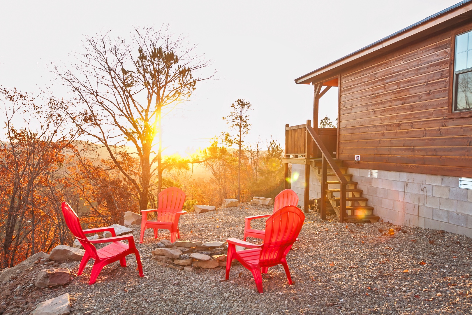 A rustic cabin with bright red chairs positioned to capture golden sunsets among autumn trees.