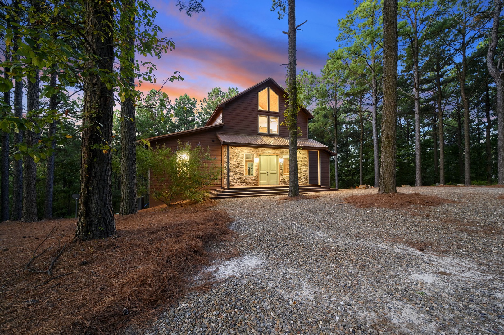 This peaceful cabin nestled among towering pines showcases beautiful stone and wood architecture, with warm lighting welcoming guests as evening settles over the forested retreat.