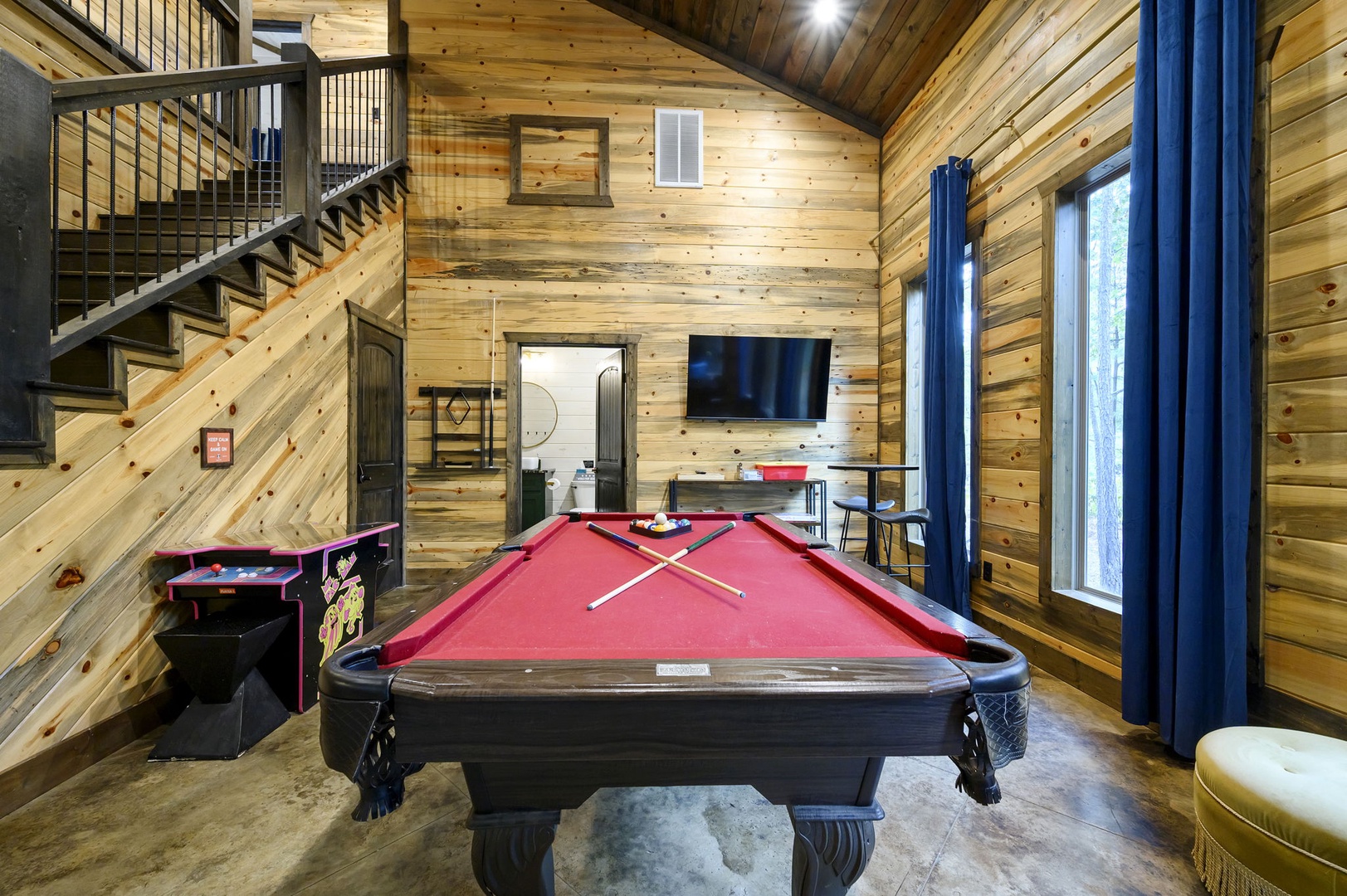 Challenge friends to a game of pool in your spacious game room, where soaring wood-beamed ceilings and natural light create a warm, inviting atmosphere for competitive fun and relaxed evenings.