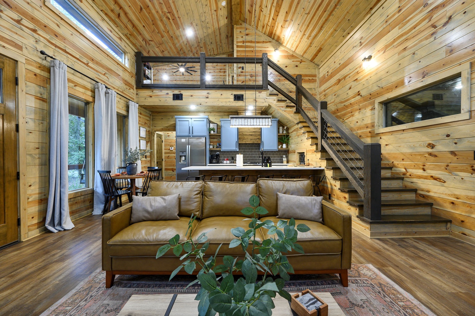 Relax in your open-concept cabin retreat with soaring wood-paneled ceilings, plush leather seating, and a fully equipped kitchen. Natural light pours through generous windows, while a lofted sleeping area adds rustic charm and extra privacy.