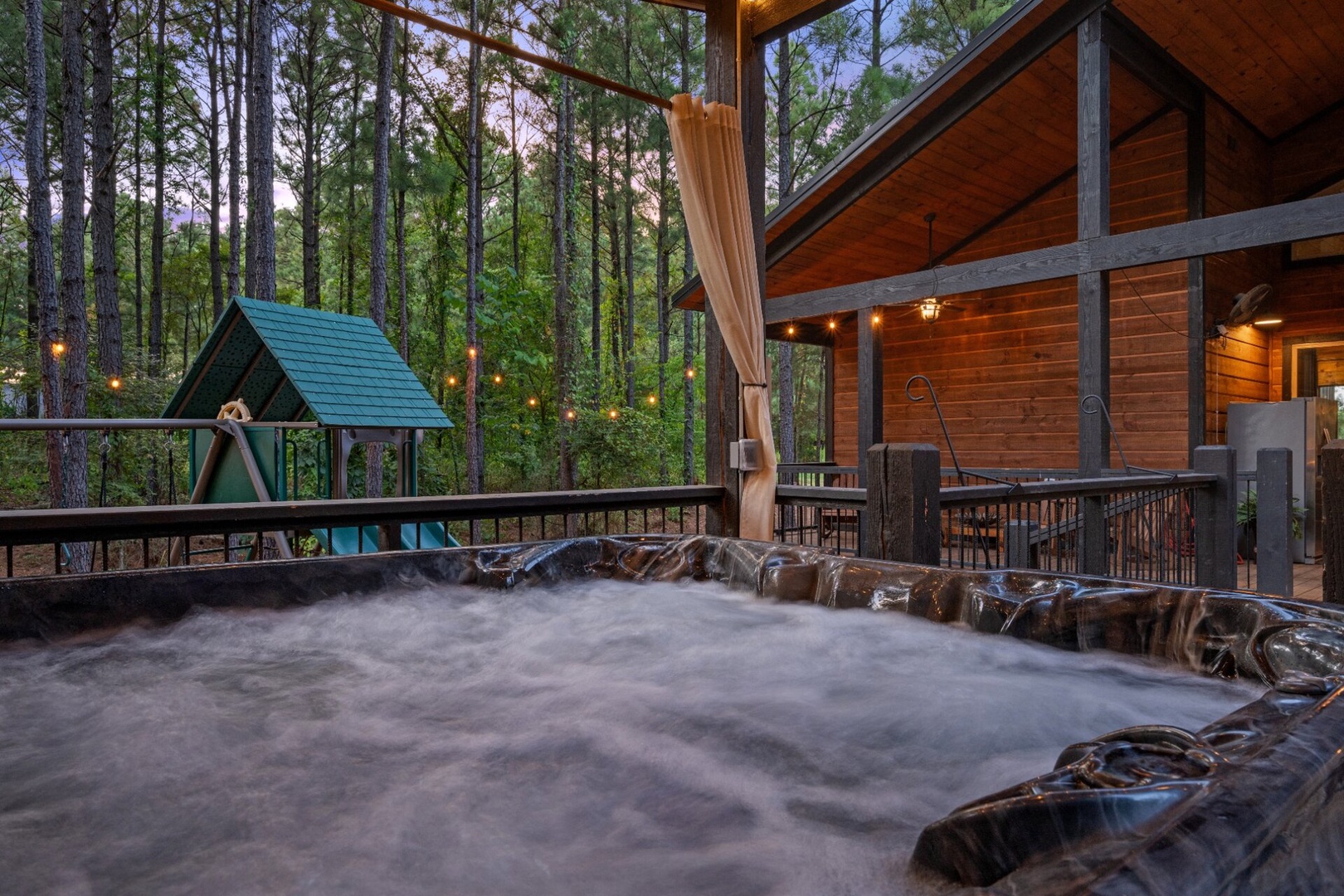 Soak in your private hot tub surrounded by towering pines, with soft lighting and a cozy cabin deck creating the perfect woodland retreat for evening relaxation.