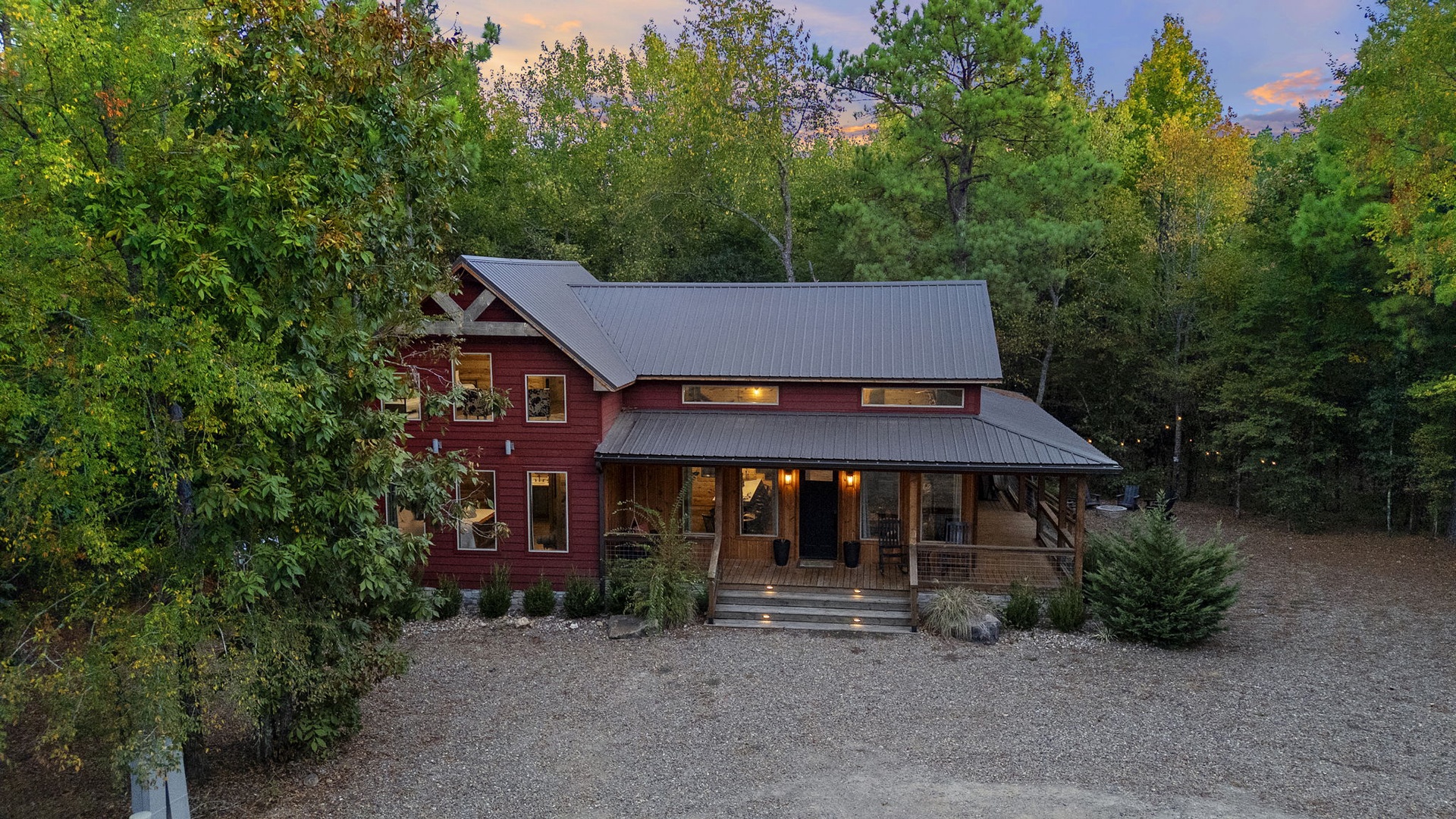 Nestled among towering evergreens and lush foliage, this charming mountain retreat welcomes guests with a warm glow and peaceful forest surroundings at twilight.
