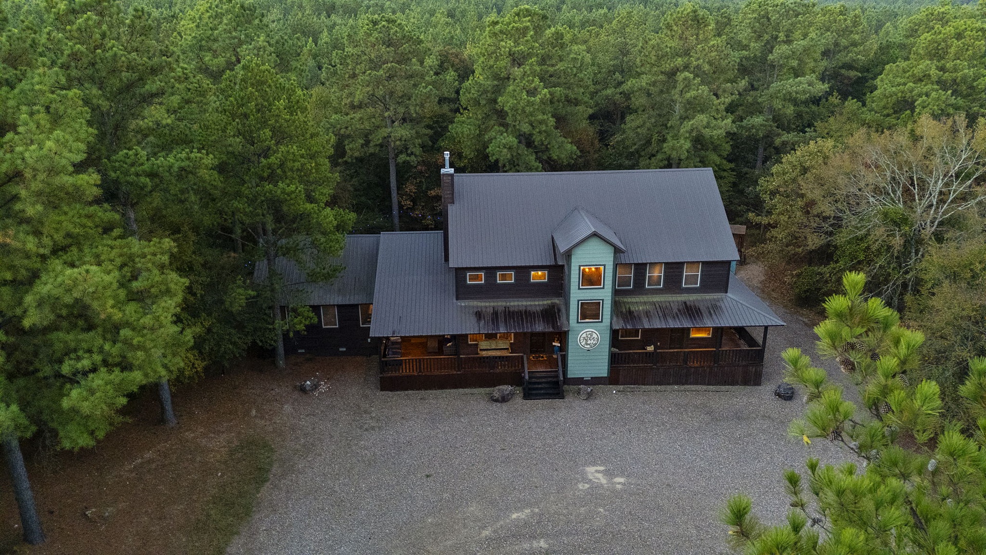 An aerial view reveals the property's rustic architecture nestled privately among lush forest surroundings, with ample parking available for arrival.