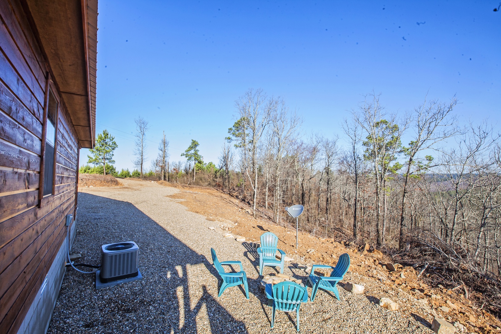 Rustic cabin exterior with hillside seating area overlooking forested valley under clear blue sky.