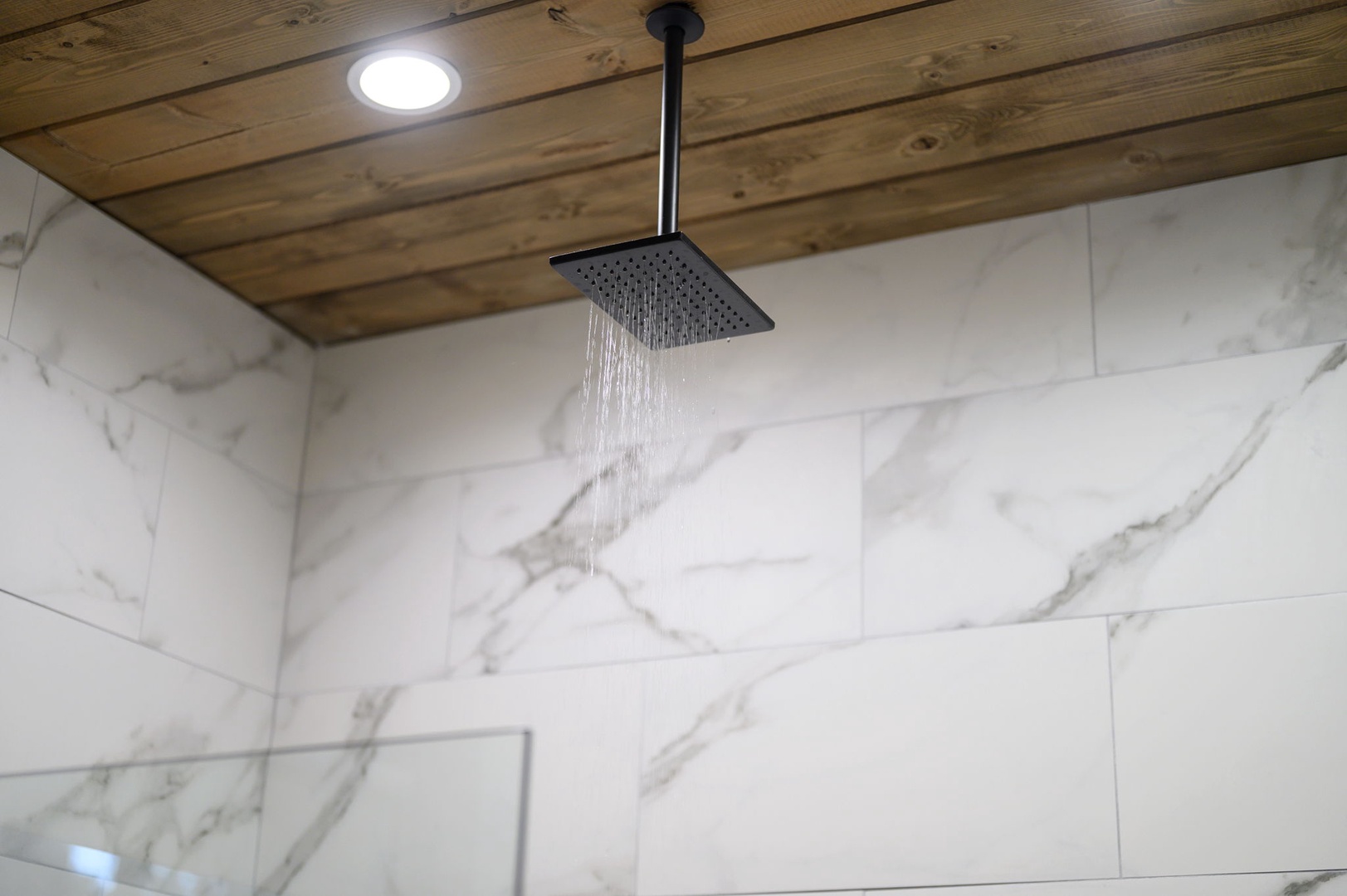 Step into your private rainfall shower with a sleek overhead design and elegant marble-look tile. The warm wood ceiling adds natural charm to your refreshing retreat.