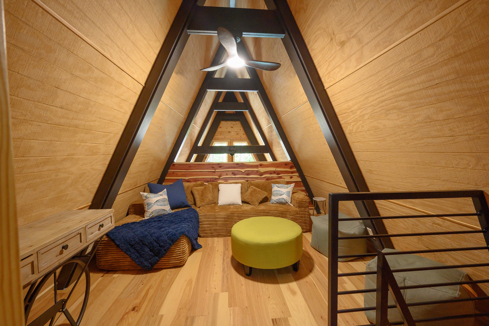 Climb up to your own cozy loft retreat, where soaring A-frame beams draw the eye skyward and warm wood wraps you in cabin charm. Sink into plush seating and unwind beneath the gentle whir of the ceiling fan.