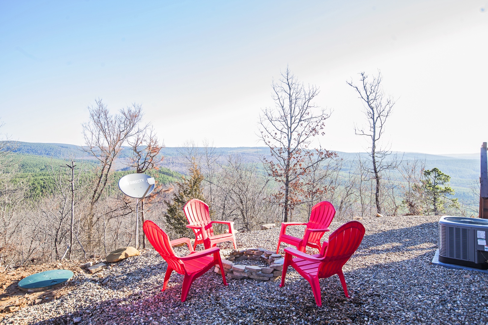 Scenic mountaintop retreat with fire pit seating area surrounded by rolling forested hills and panoramic valley views.
