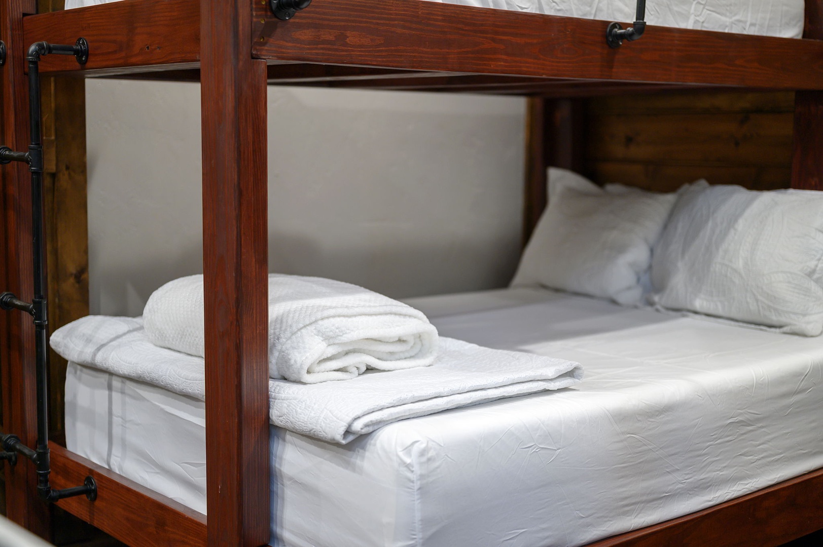 Crisp white linens and plush towels await your arrival, thoughtfully arranged atop this inviting bunk bed framed in rich, warm wood.