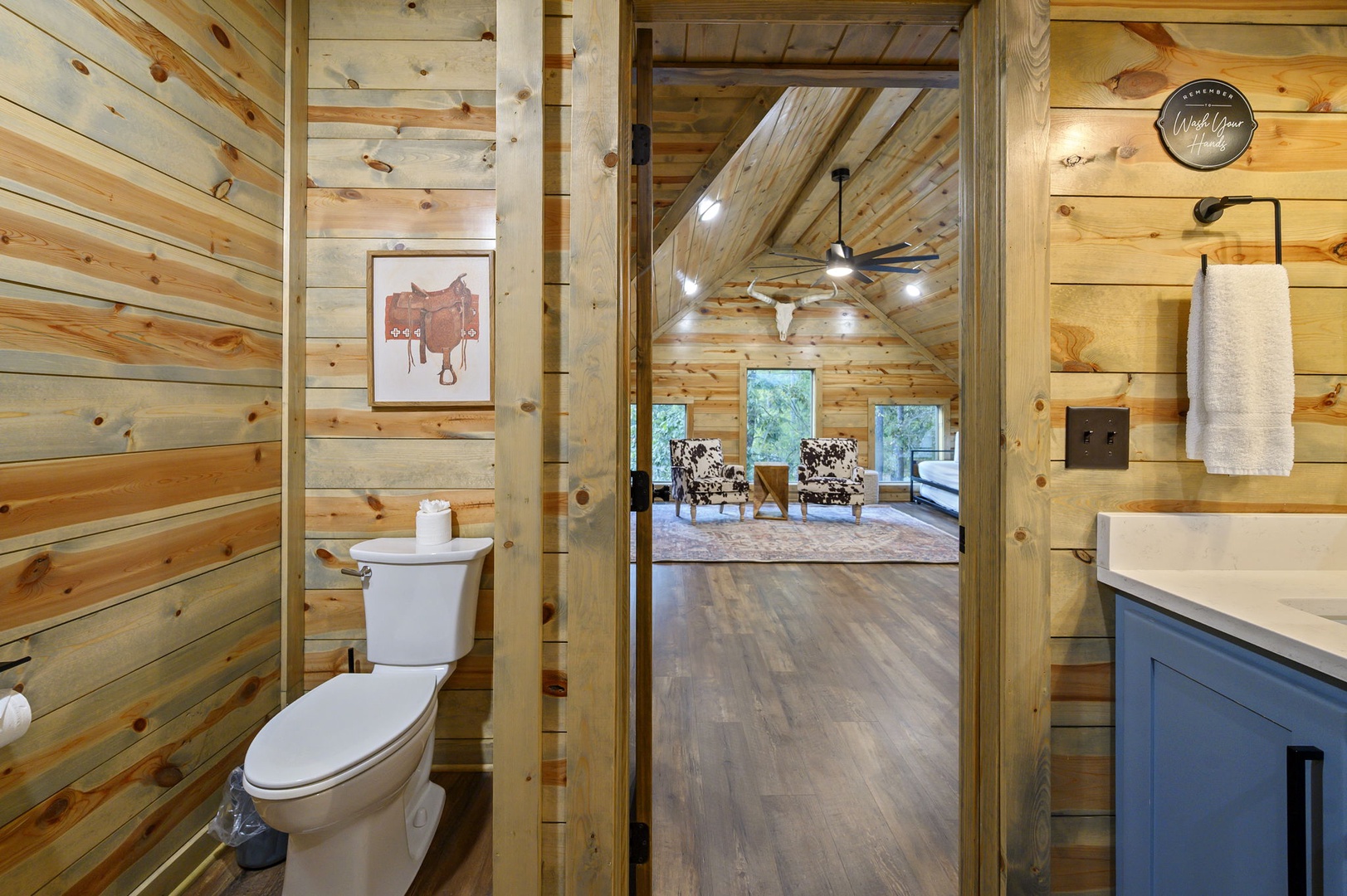 Rustic charm meets modern comfort in your bathroom with warm wood paneling, farmhouse fixtures, and a peaceful glimpse into the inviting living space beyond.