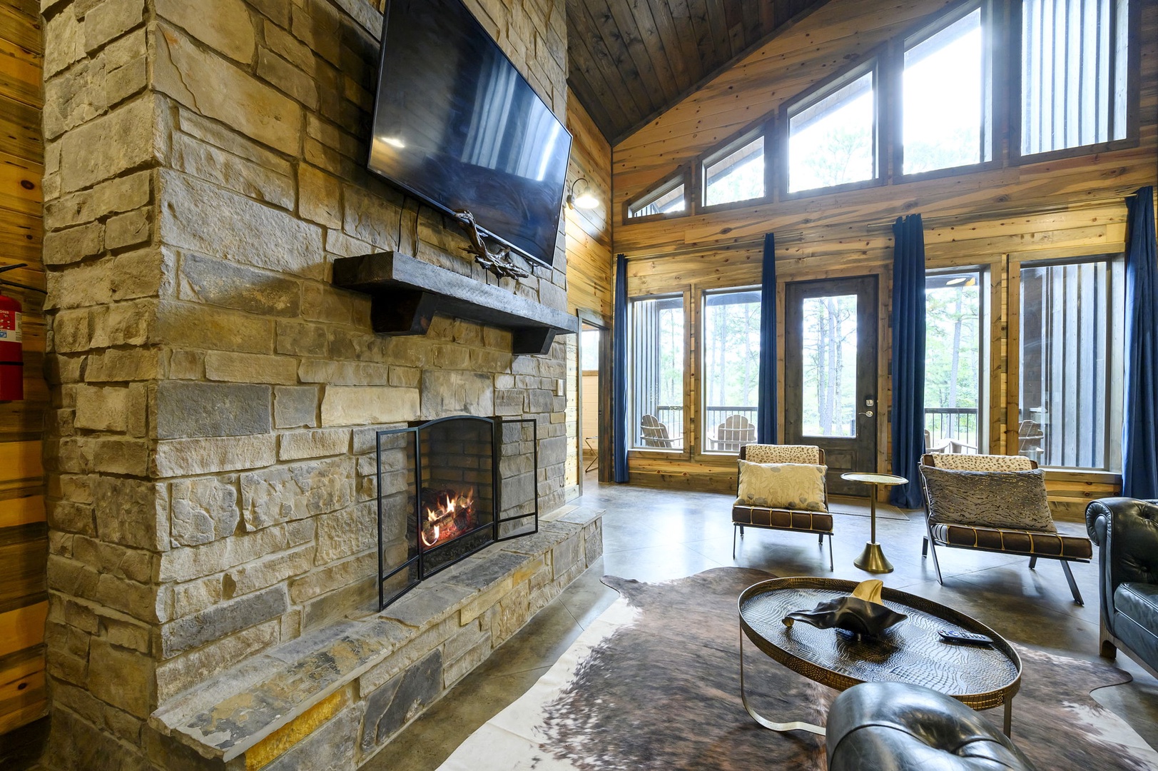 Unwind in your living room's warm embrace, where the stone fireplace crackles invitingly and soaring windows frame the natural beauty beyond, creating the perfect retreat.