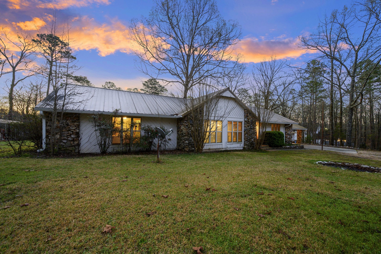 Modern farmhouse with stone accents nestled among towering trees, featuring warm lighting and peaceful surroundings for your countryside retreat.