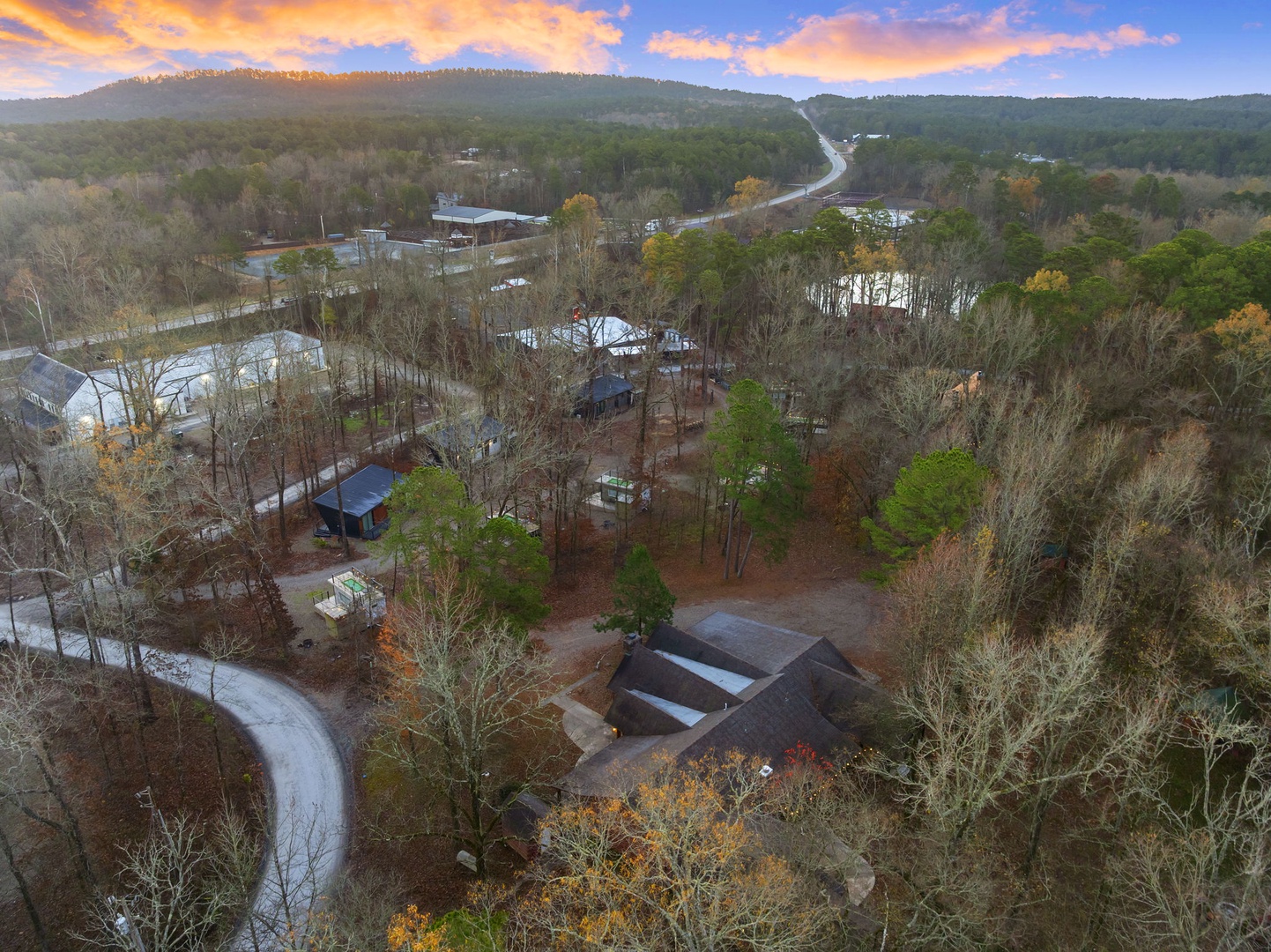 Stunning aerial view of this peaceful mountain retreat nestled among rolling hills and vibrant autumn foliage at sunset.