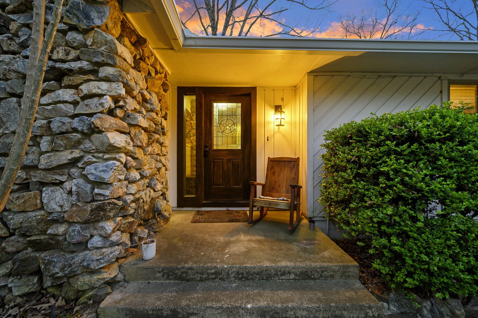 Welcoming stone and wood entrance with charming rocking chair where twilight creates the perfect arrival ambiance.