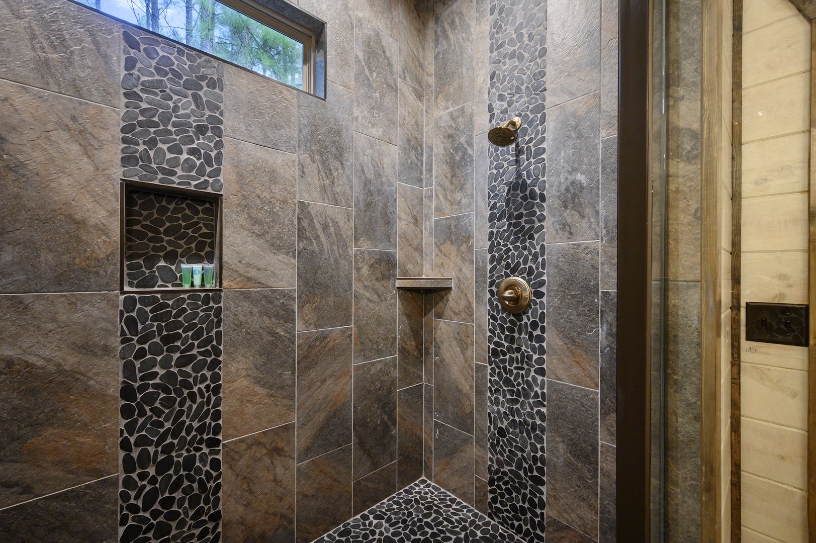 Step into a spa-like retreat with natural stone tile, pebble accents, and a built-in shelf for your essentials—your perfect place to unwind.