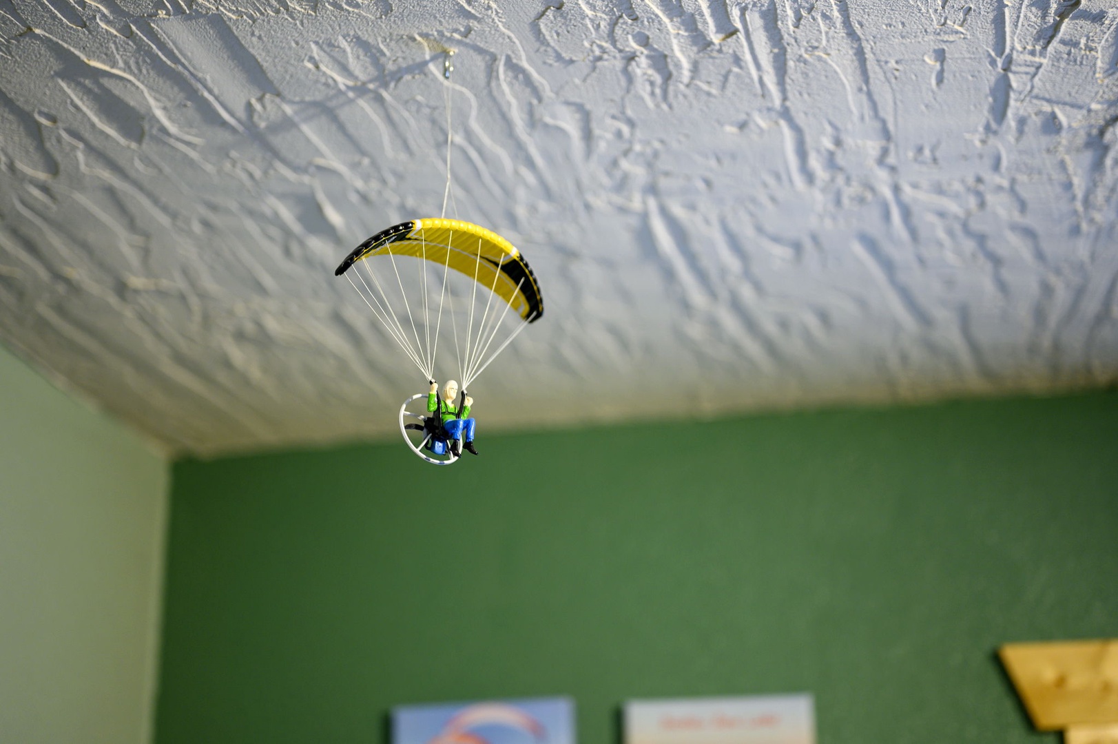 A whimsical miniature paraglider hangs from your ceiling, adding playful adventure vibes to this cozy green room.