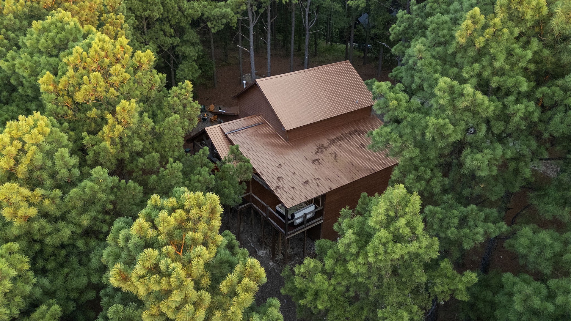 Aerial view of a secluded cabin nestled among lush forest, offering a peaceful retreat surrounded by nature's vibrant canopy.