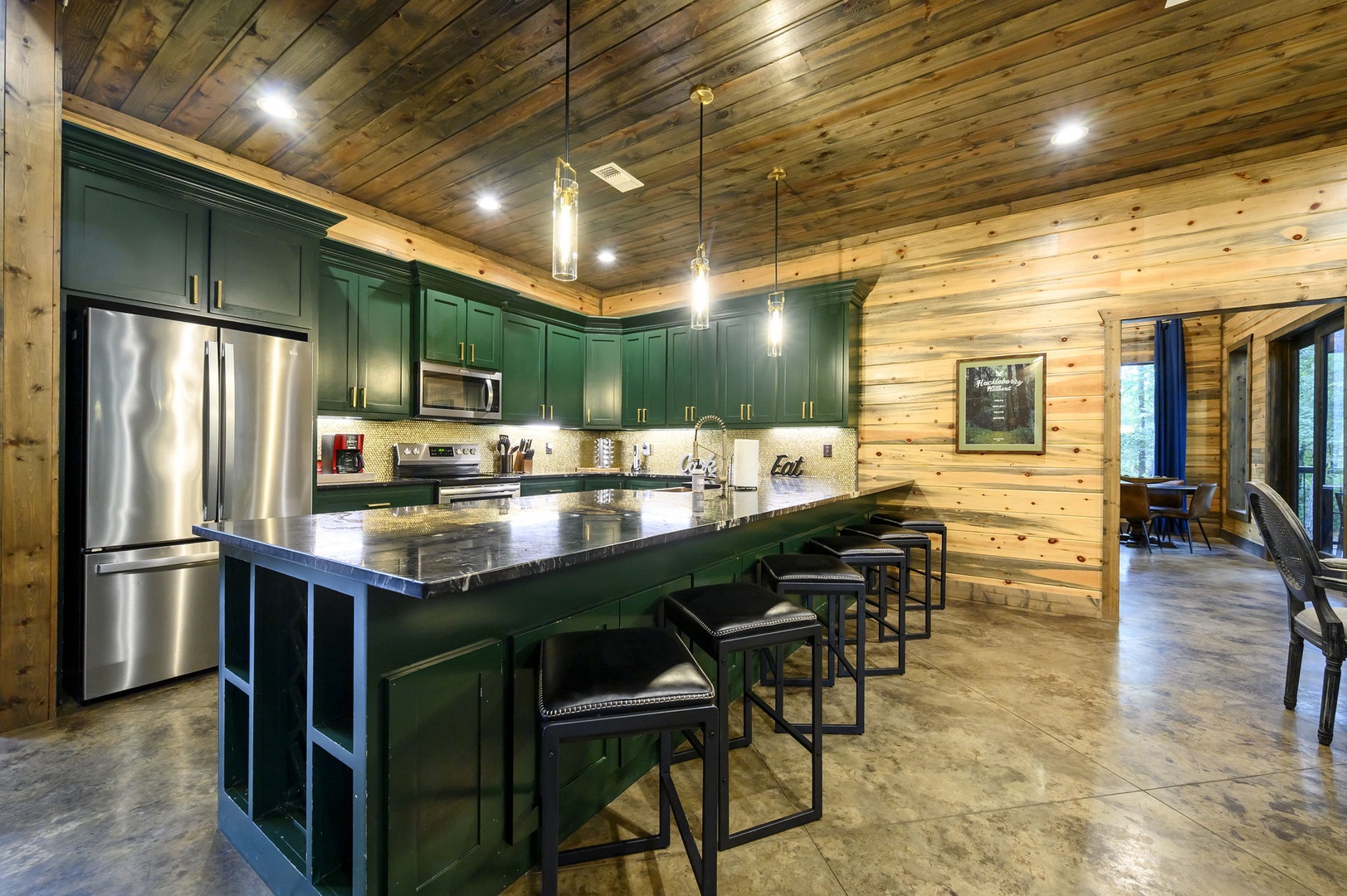 Gather around this spacious kitchen island, where deep emerald cabinetry and gleaming countertops invite you to cook, share meals, and create vacation memories beneath warm wood-planked ceilings.