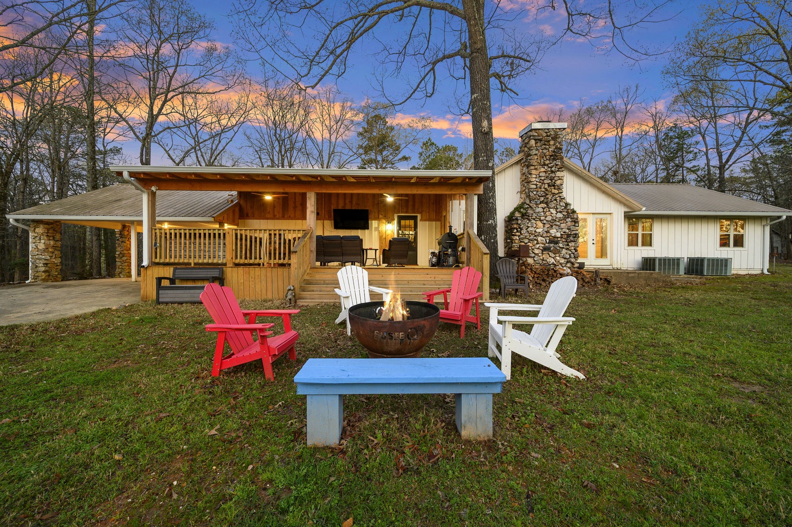Charming lakeside retreat featuring a stone fireplace, covered deck, and colorful Adirondack chairs around a fire pit for memorable evenings.