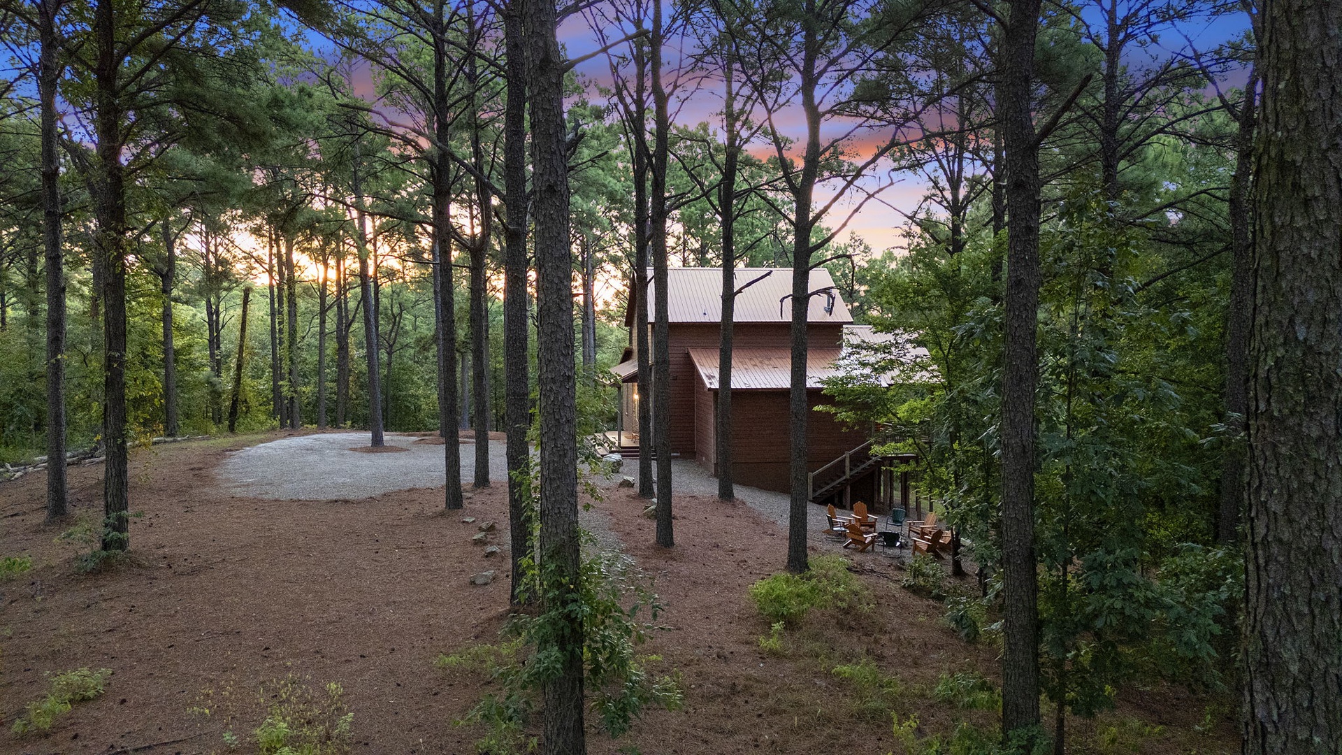 A secluded cabin nestled among tall pines captures the serene glow of dusk, with outdoor seating ready for peaceful evenings beneath the trees.