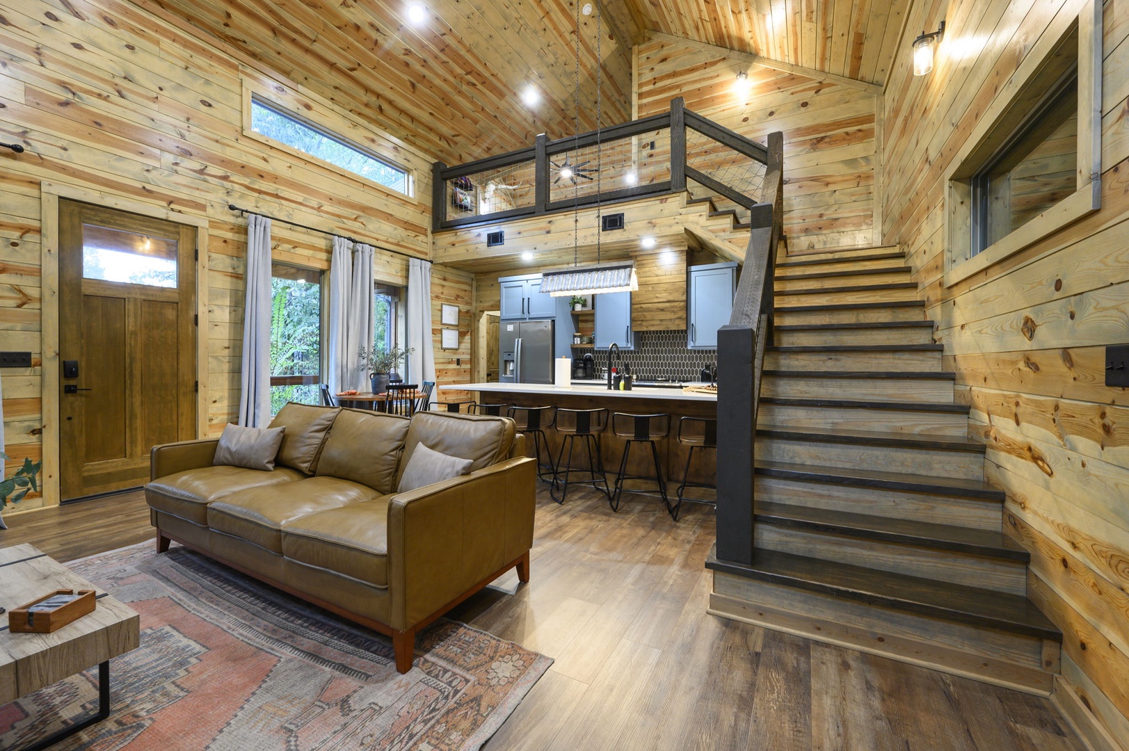 Step into your cozy retreat where warm wood surrounds you and modern comfort meets rustic charm. The open layout invites you to relax on the leather sofa, whip up a meal in the sleek kitchen, or explore the loft above—all within one beautiful space.