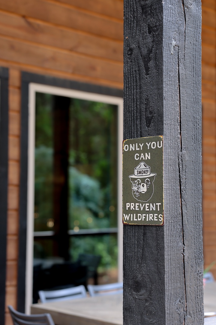 A classic Smokey Bear sign greets visitors at the property entrance, set against warm wood siding with natural surroundings visible in the background.