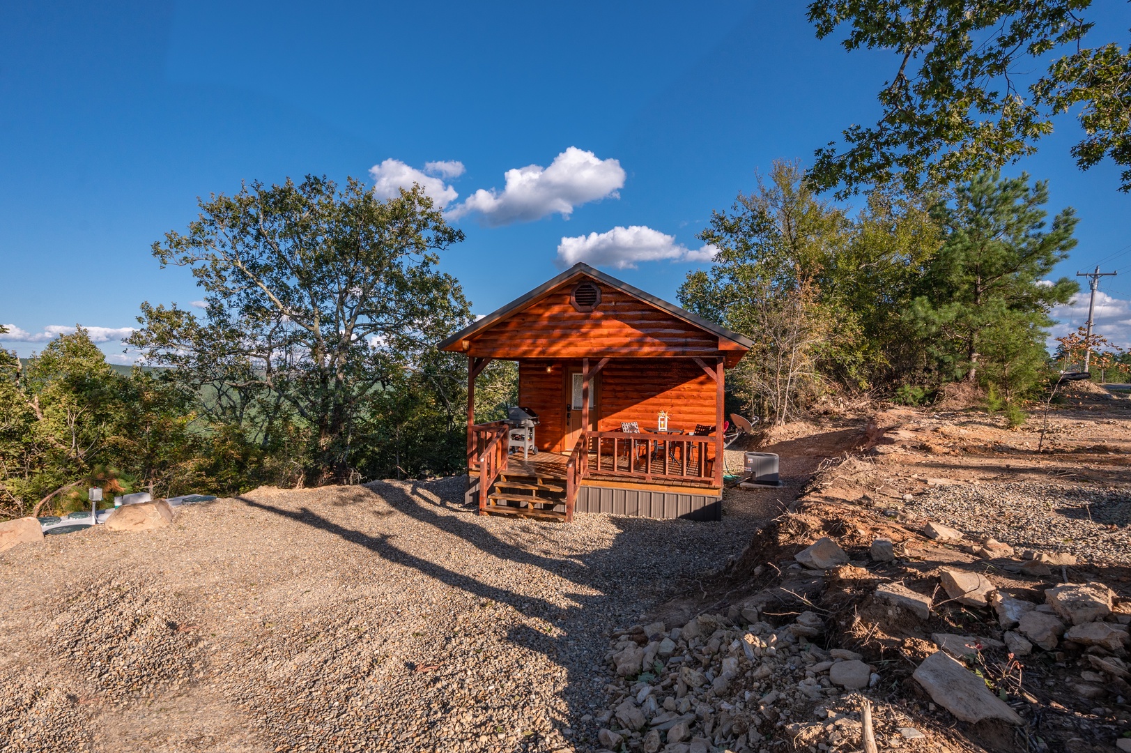Rustic wooden cabin nestled among mature trees offers peaceful retreat with covered porch and natural stone surroundings.