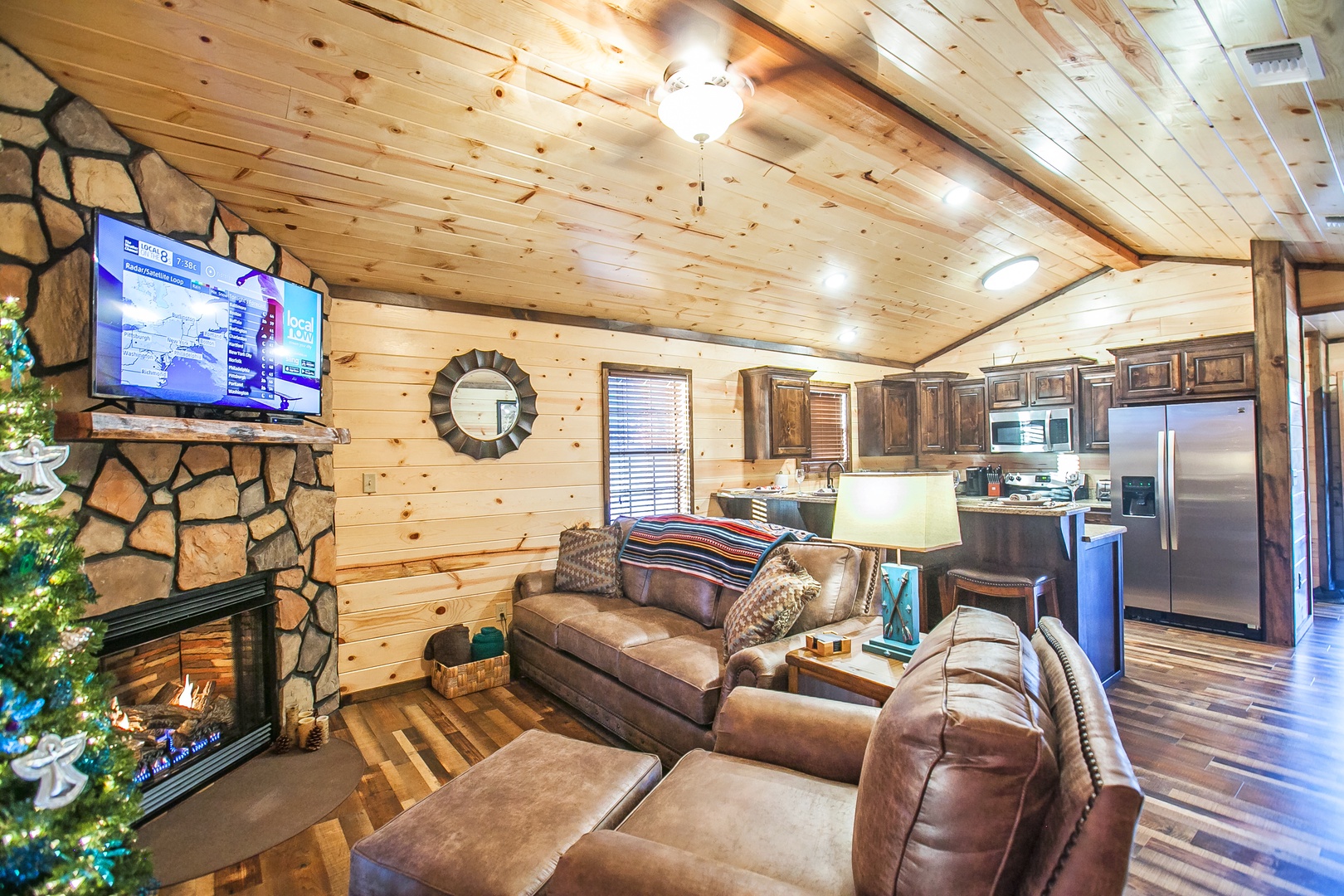 Unwind in your rustic living room with stone fireplace, cozy leather seating, and open kitchen - perfect for mountain evenings together.
