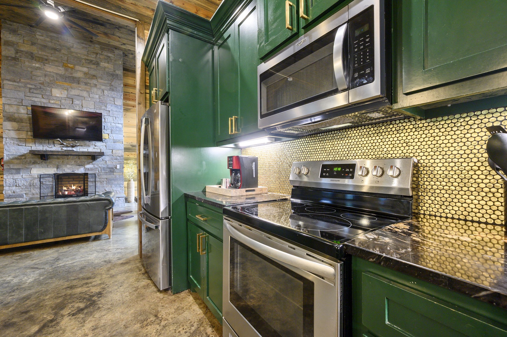 Step into your stylish kitchen with bold emerald cabinetry, gleaming stainless appliances, and a stunning honeycomb-tile backsplash that catches the light. The cozy fireplace beyond invites you to unwind after preparing your favorite meal.