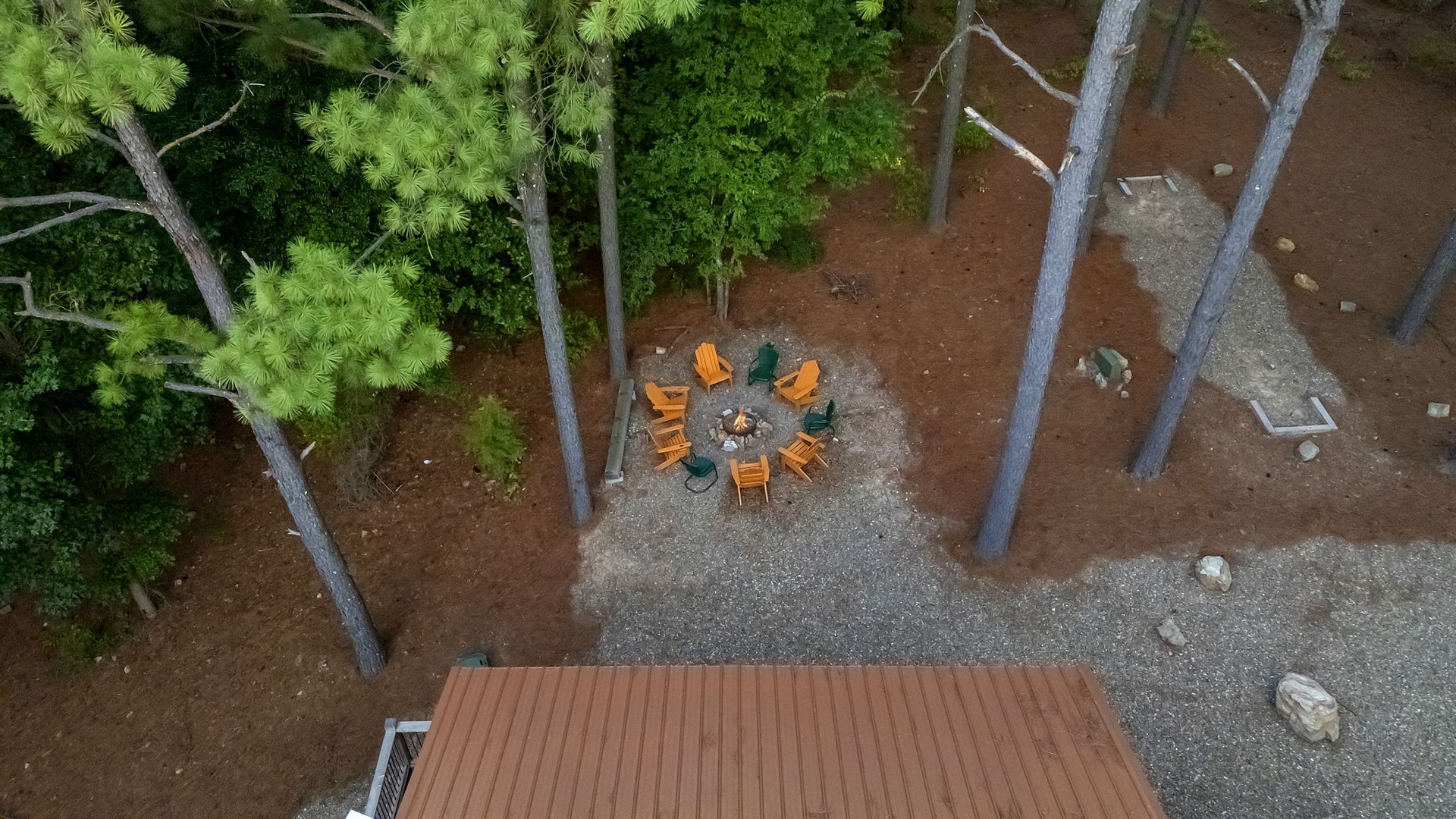 Aerial view of the property's outdoor fire pit area surrounded by towering pines and natural woodland, offering a peaceful gathering spot in the forest setting.