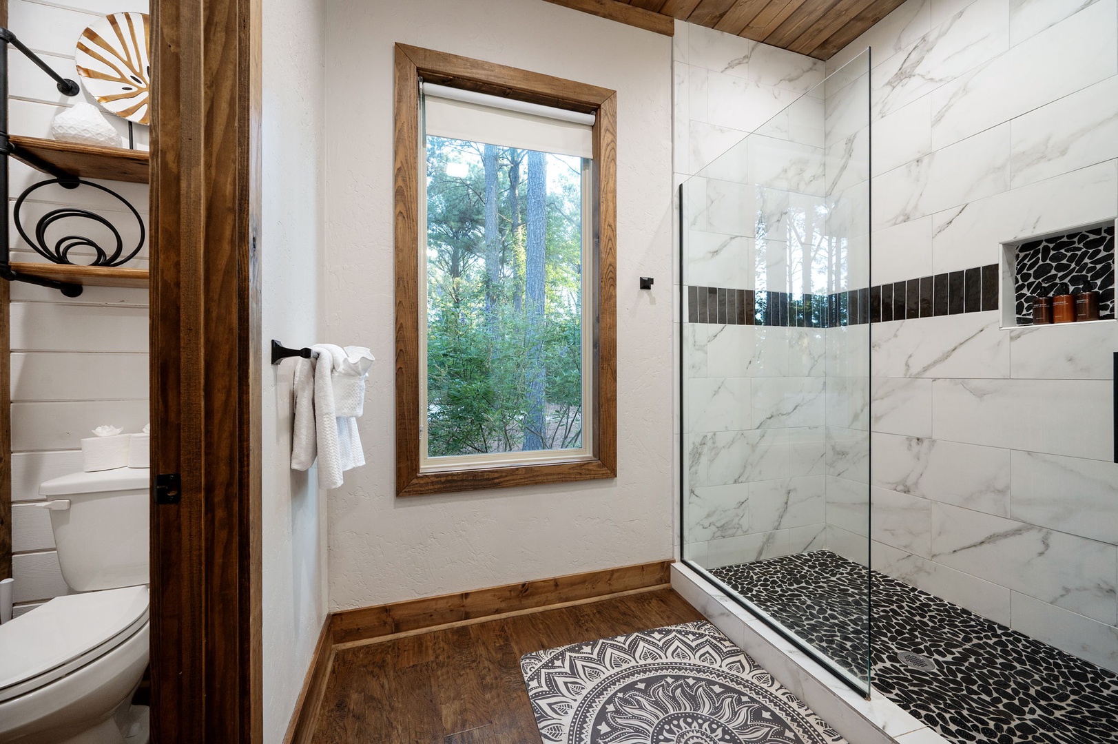 Step into your spa-like retreat with a stunning marble walk-in shower, warm wood accents, and a serene view of nature through the window—your perfect place to refresh and unwind.