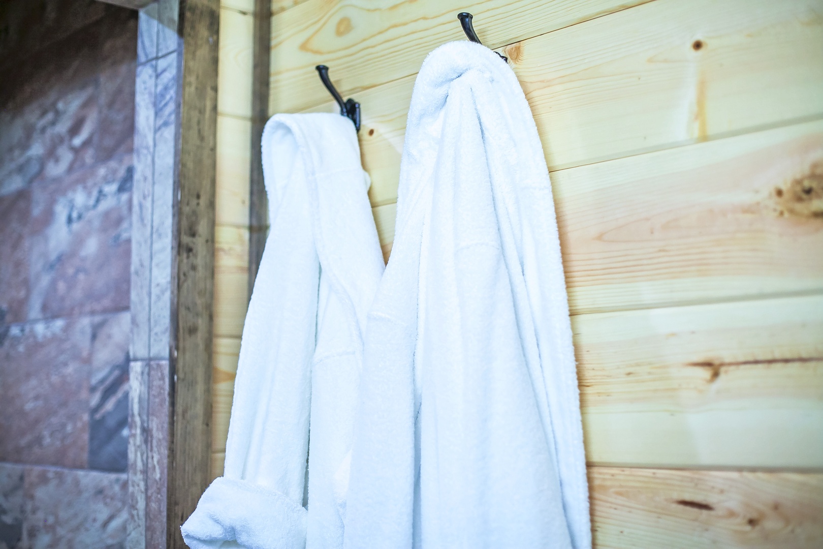 Plush bathrobes await you after a relaxing soak, hanging ready on warm wooden walls for ultimate comfort and luxury.