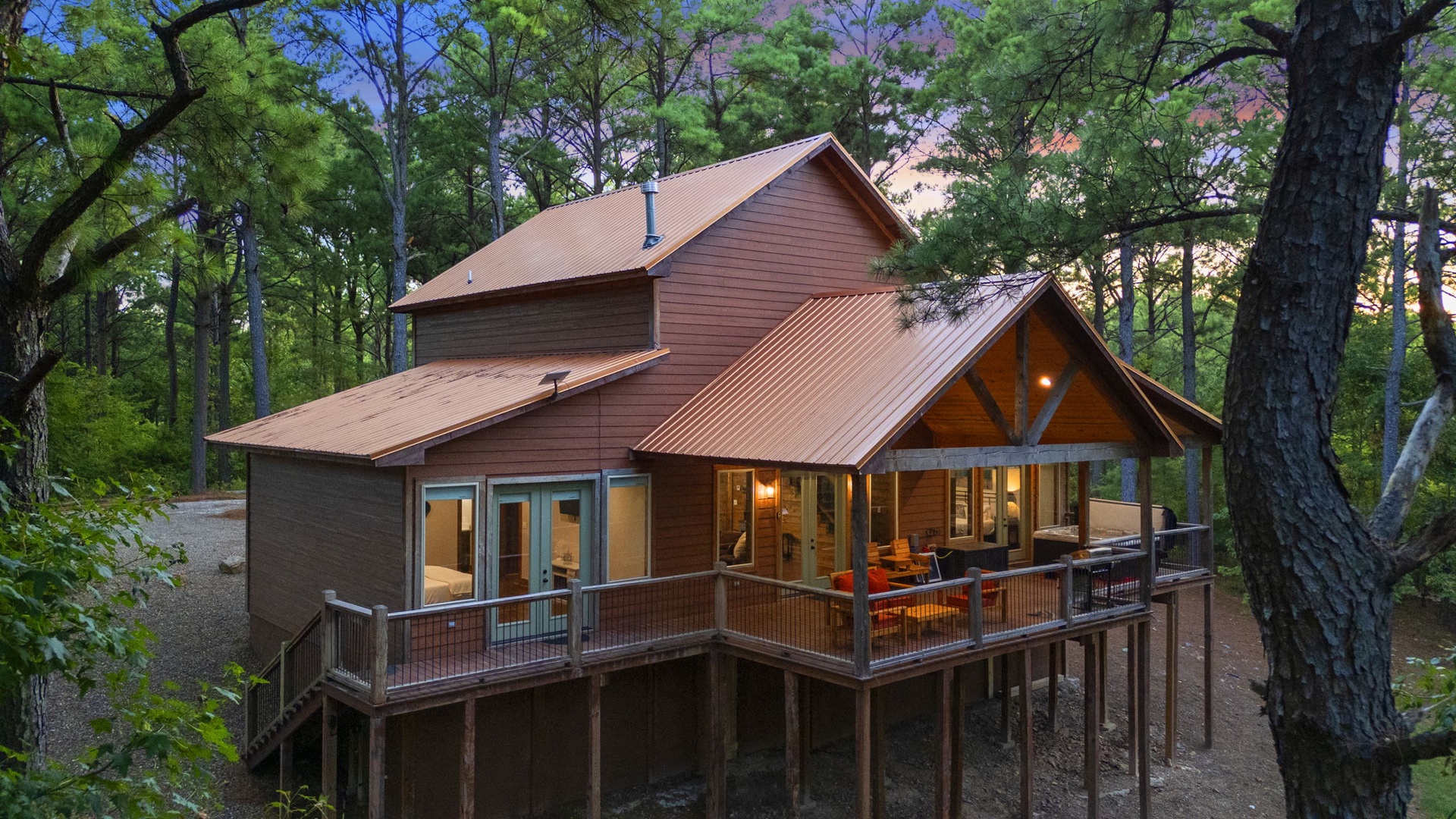 A charming cabin nestled among tall trees, featuring a spacious deck perfect for enjoying peaceful forest surroundings at sunset.