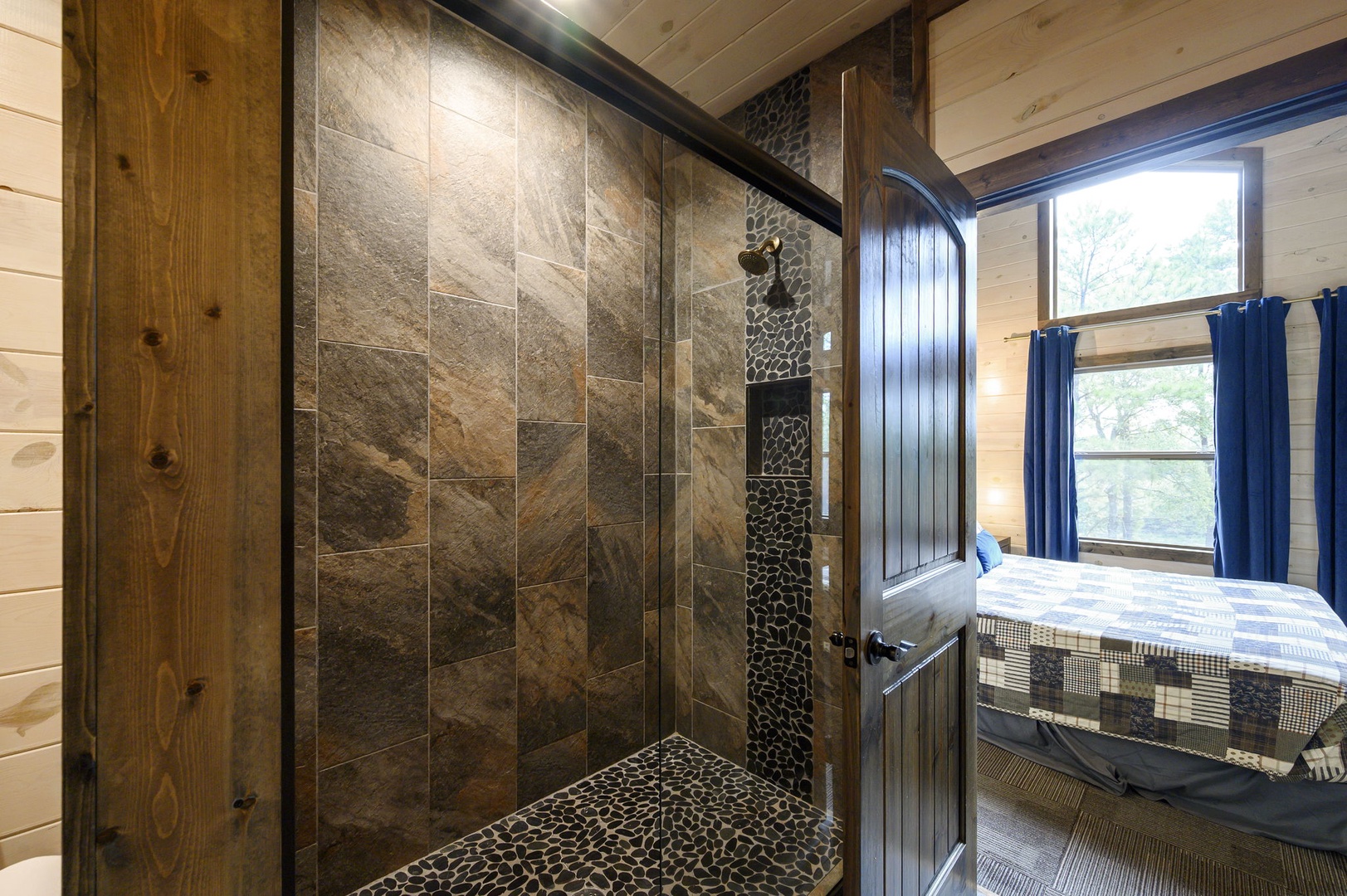 Your private retreat features a luxurious stone-tiled shower with natural light streaming in, framed by warm wood accents that echo the peaceful forest views just outside your window.