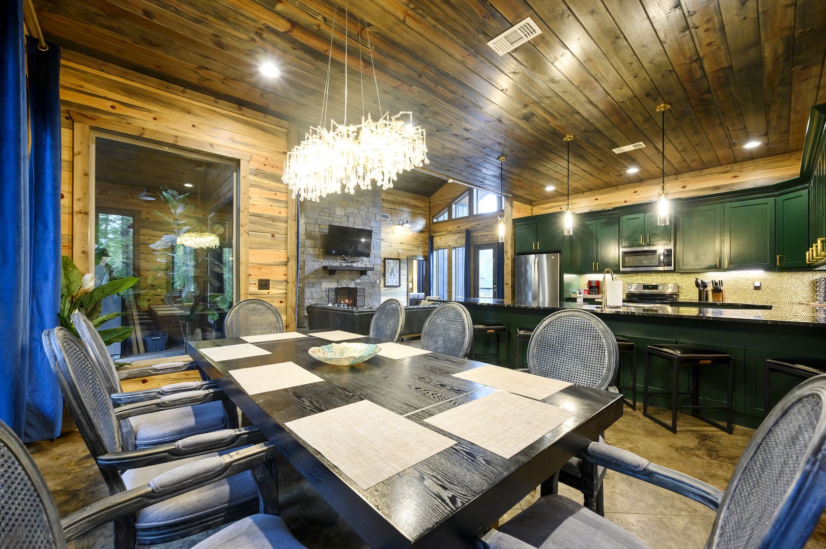 Gather around the handsome dining table under a stunning chandelier, with the open kitchen ready for your group meals and warm wooden ceilings creating a welcoming mountain retreat atmosphere.