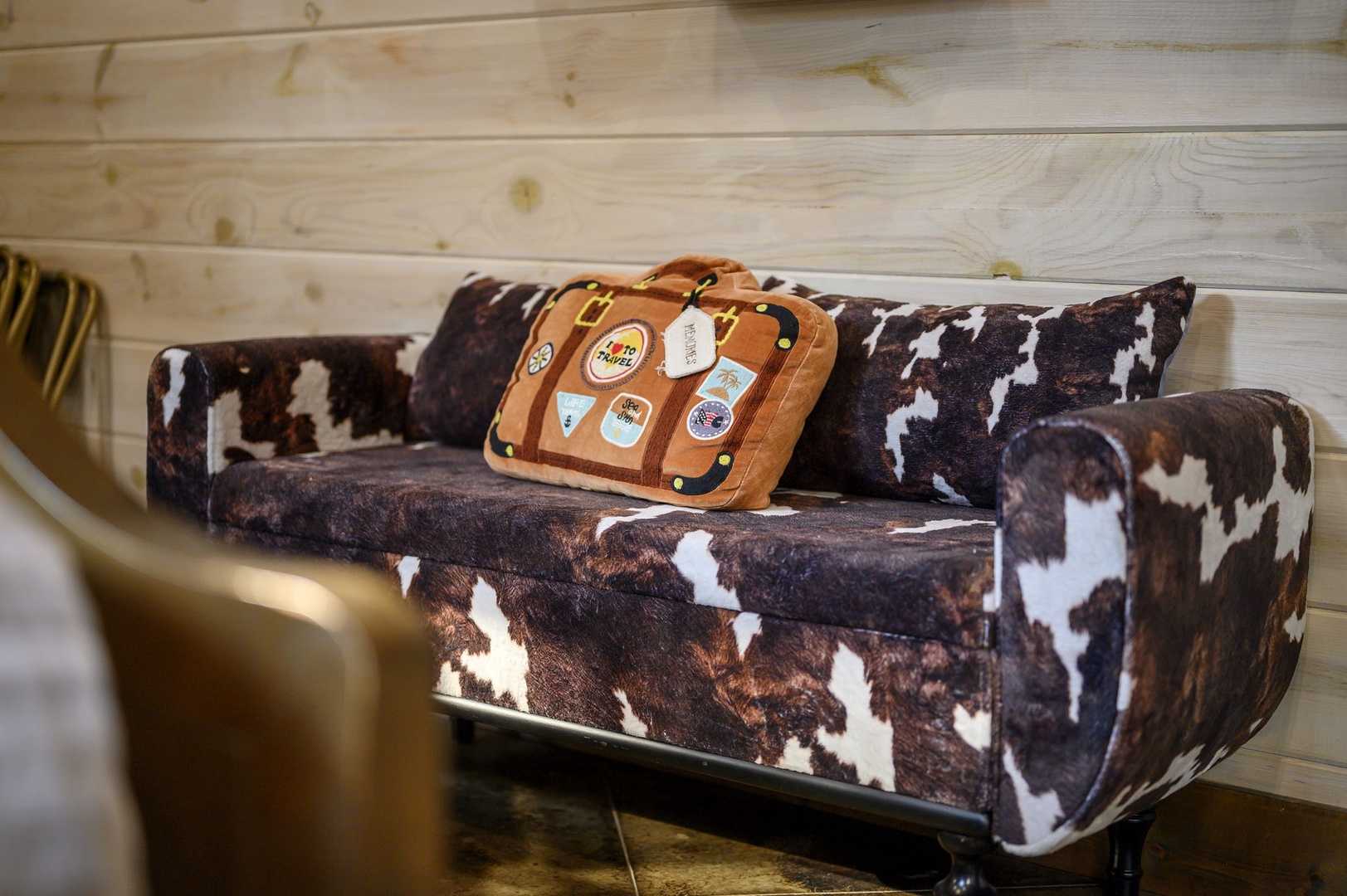 Settle into a cozy cowhide loveseat with playful travel-themed pillows, perfect for swapping stories after a day of adventure. The warm wood paneling adds rustic charm to your retreat.