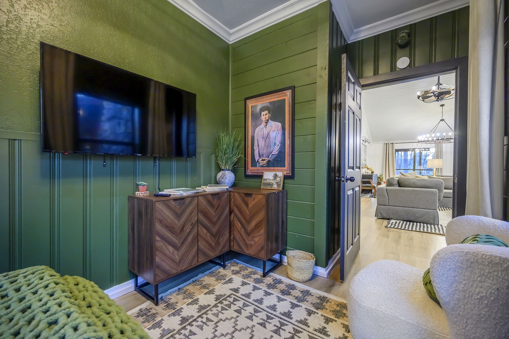 Unwind in your stylish living space featuring rich green walls, a mounted TV, and elegant furnishings that create the perfect atmosphere for relaxation.