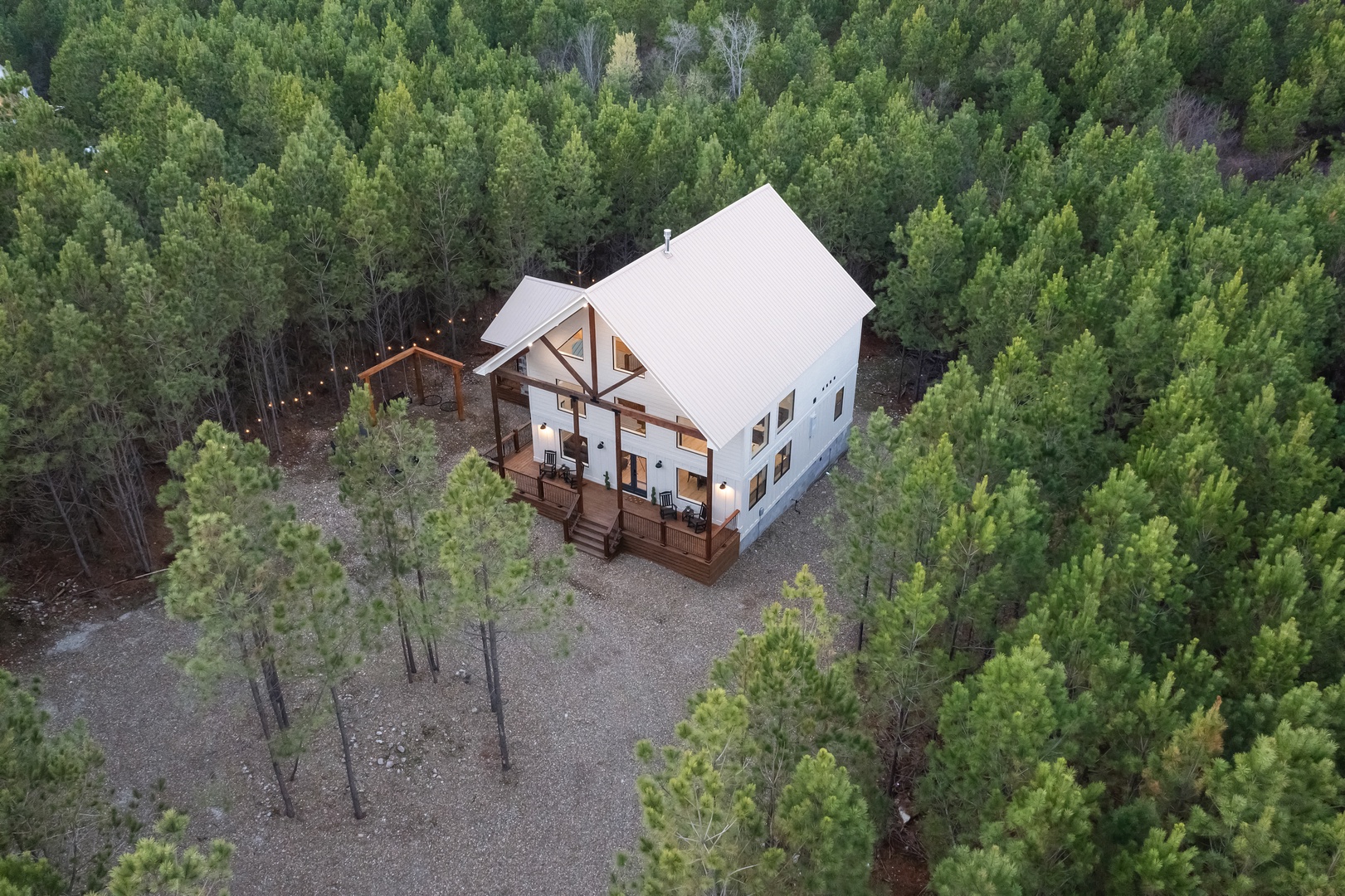 A modern cabin retreat nestled in pristine forest, featuring spacious decks and warm lighting surrounded by towering trees.