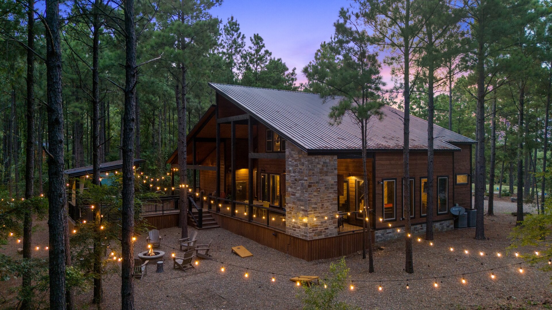 A charming cabin nestled among towering pines, with warm string lights creating an inviting glow as dusk settles in.