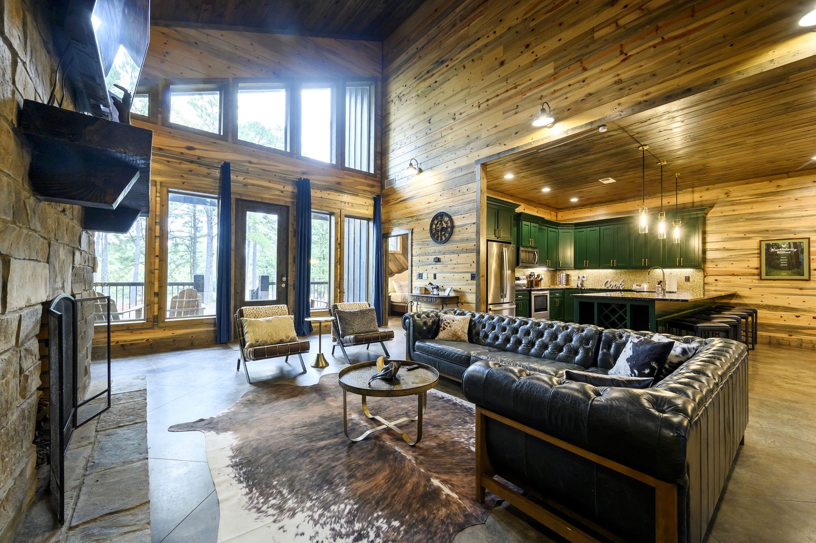 Sink into the tufted leather sofa and let the warmth of the stone fireplace embrace you. Floor-to-ceiling windows frame the surrounding woods, filling this stunning open-plan space with natural light and a sense of peaceful escape.