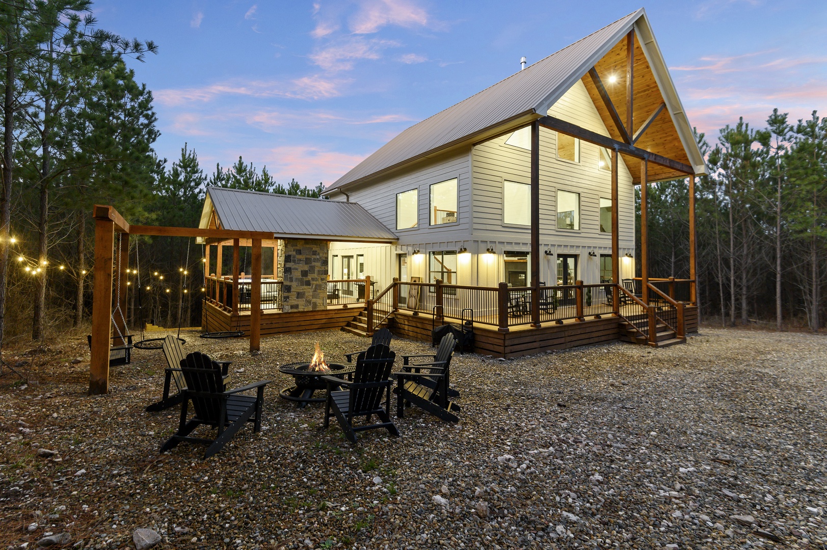 Modern cabin retreat surrounded by forest, featuring wraparound deck, fire pit, and swing set for the perfect woodland escape.