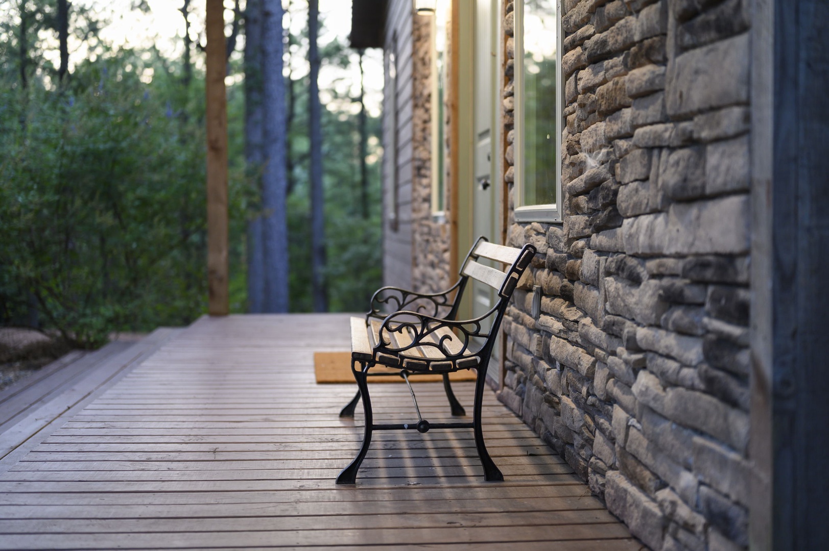 A peaceful wooden deck wrapped in tall forest pines offers an inviting bench to relax and soak in the mountain escape. The stone and timber setting creates a naturally cozy retreat.