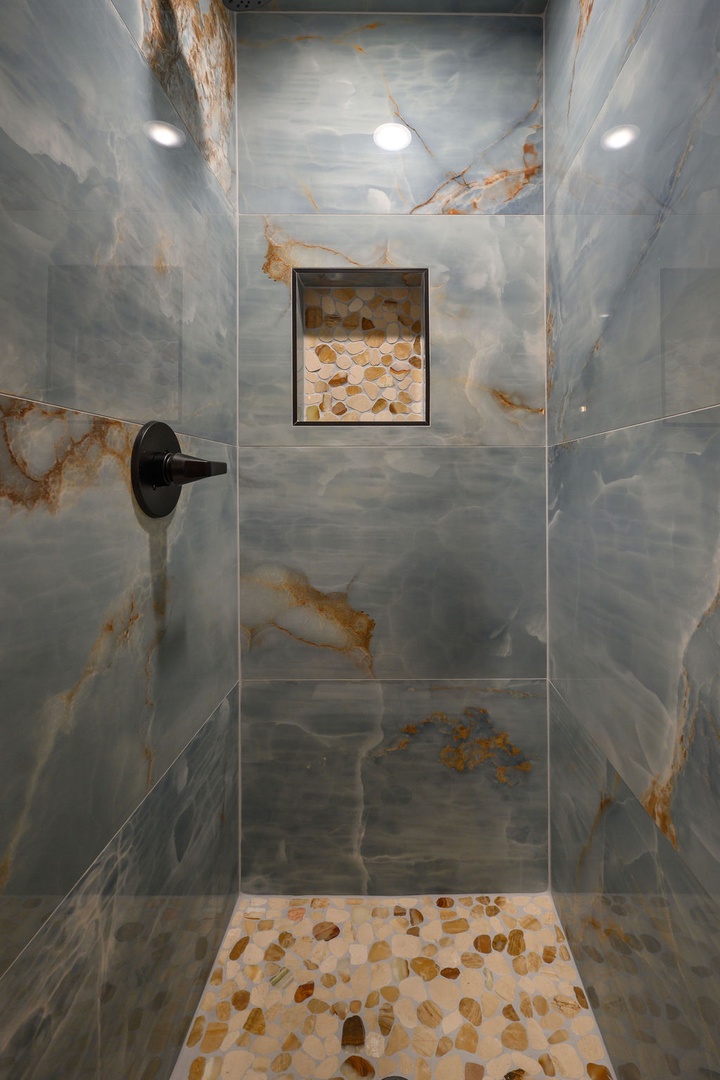 Step into a spa-like sanctuary featuring stunning marble-look walls and a natural river stone floor that massages your feet with every step. The recessed niche adds a designer touch.