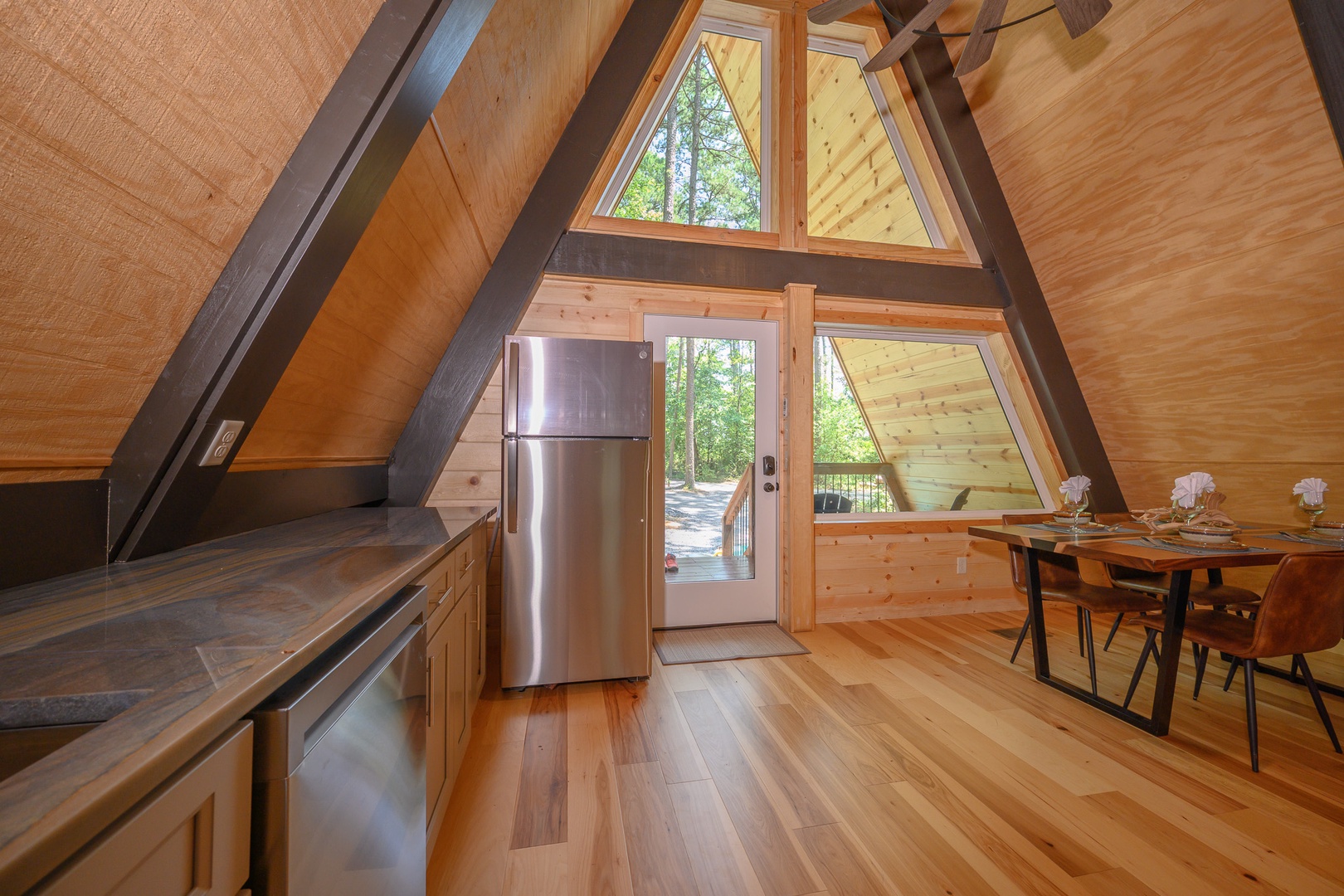 Step into your cozy A-frame retreat, where warm wood walls and soaring ceilings create an inviting mountain escape. Natural light floods through expansive windows, while your fully equipped kitchen and dining space await for memorable meals together.