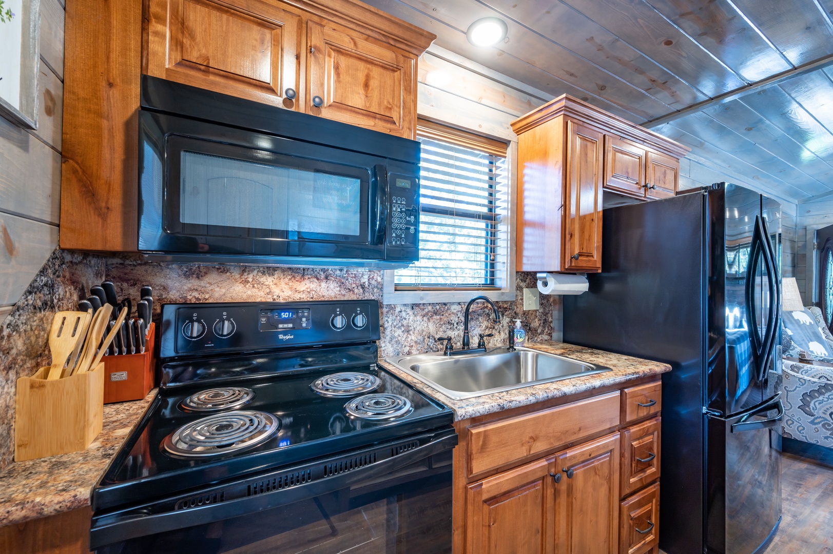 Cook with ease in your fully-equipped kitchen featuring granite counters, warm wood cabinets, and modern black appliances.